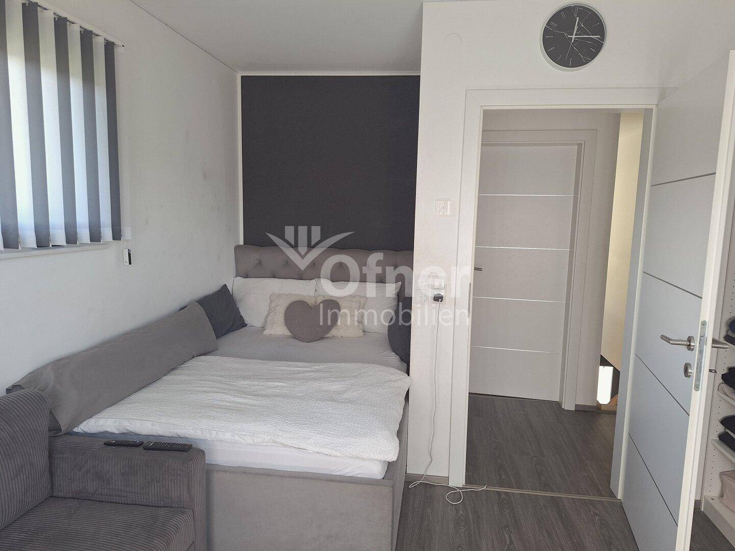 Gemütliches Schlafzimmer mit Bett, dunkler Akzentwand und Zugang zu einem weiteren Raum.