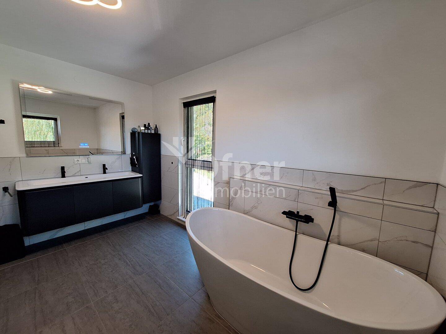 Großes, modernes Badezimmer mit freistehender Badewanne, Doppelwaschbecken und Fenster.
