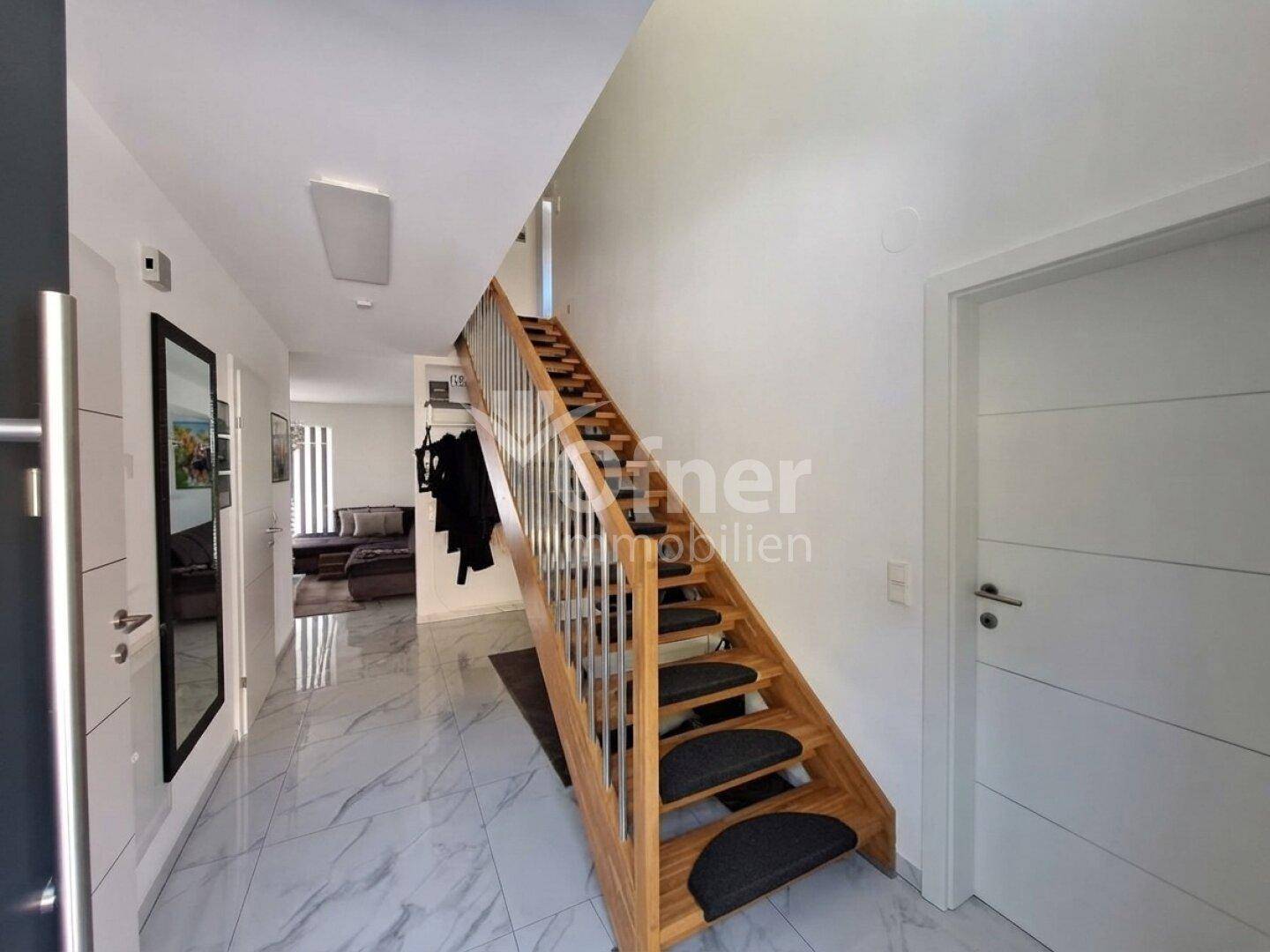 Heller Eingangsbereich mit moderner Holztreppe, Fliesenboden und Zugang zu weiteren Räumen.
