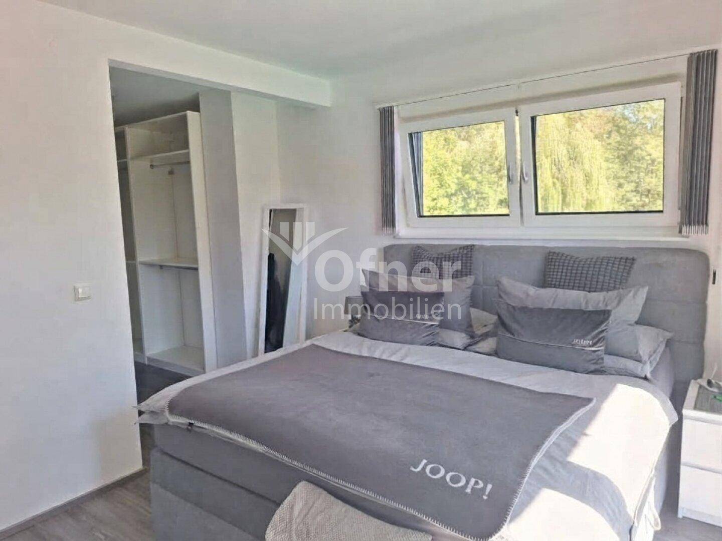 Gemütliches Schlafzimmer mit Doppelbett, Holzboden und Blick ins Grüne durch große Fenster.