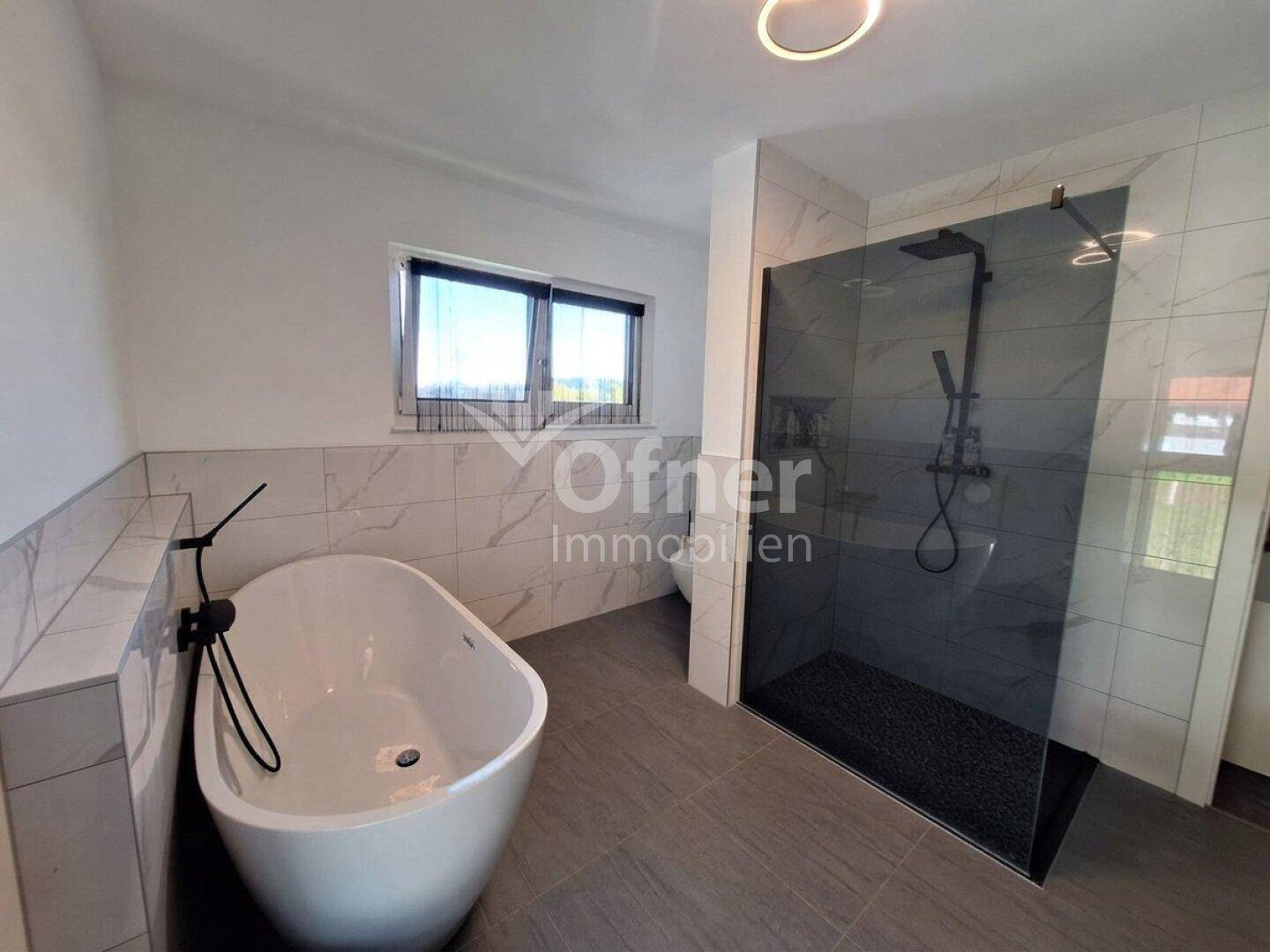 Elegantes Badezimmer mit freistehender Badewanne, großer begehbarer Dusche und modernen Fliesen.
