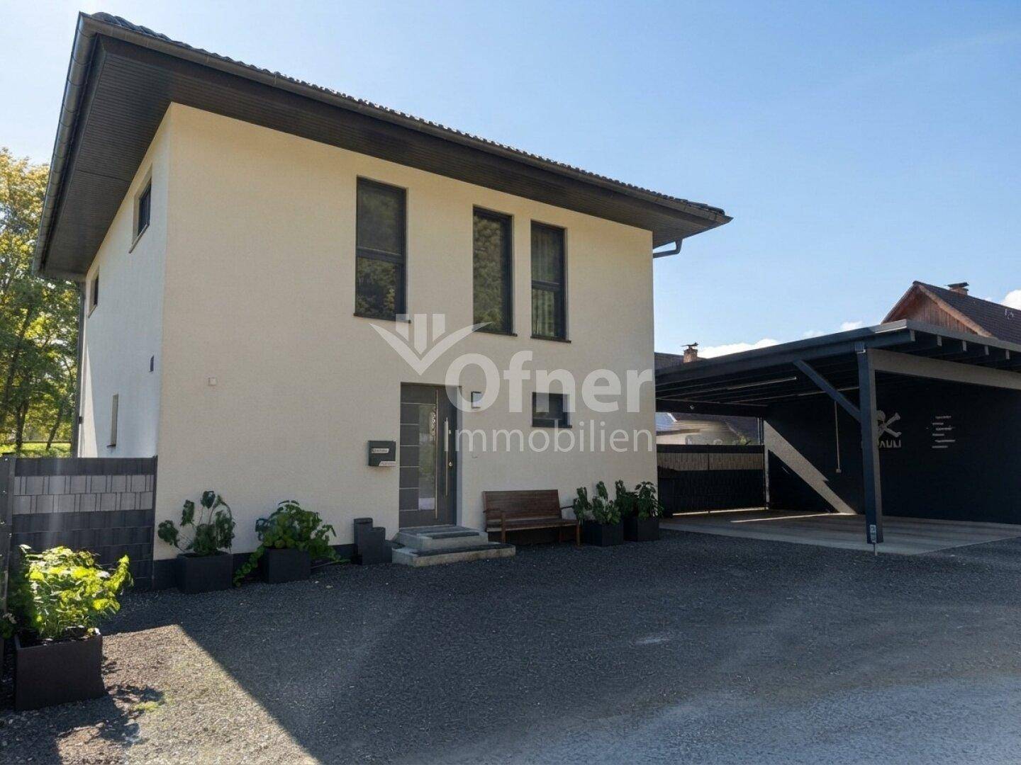 Modernes Einfamilienhaus mit heller Fassade, Carport und gepflegter Zufahrt.