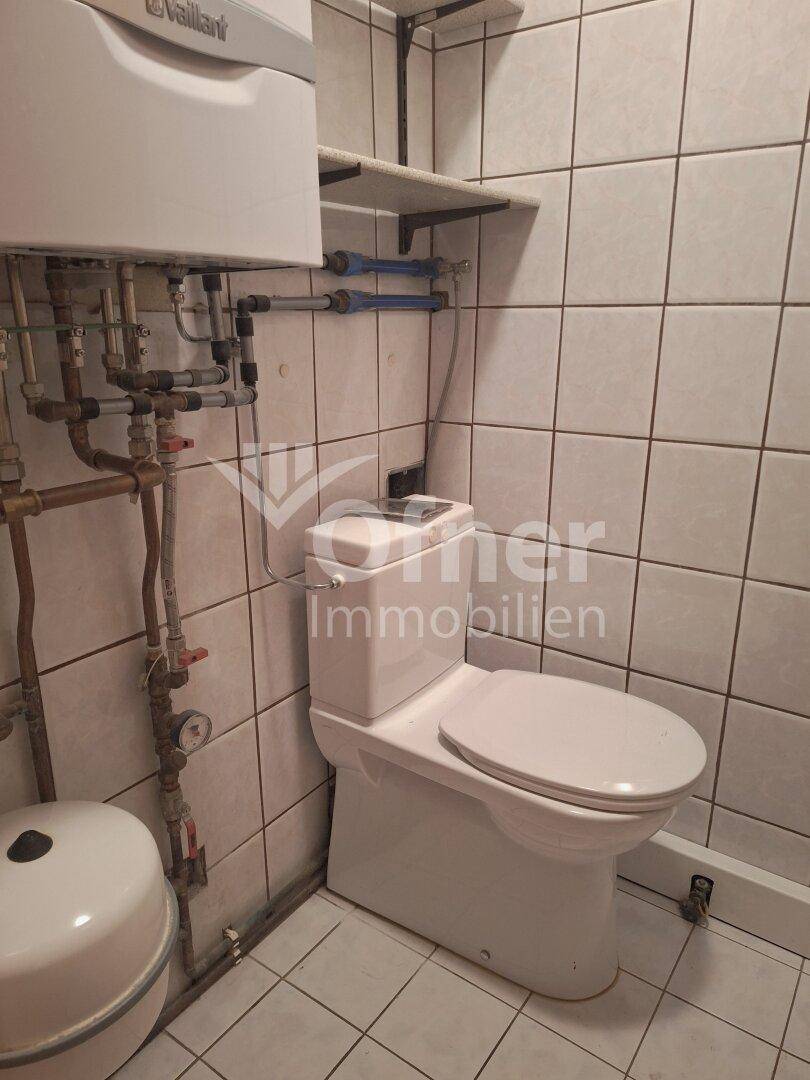 Kleines WC mit Toilette, Fliesen und sichtbaren Installationen.