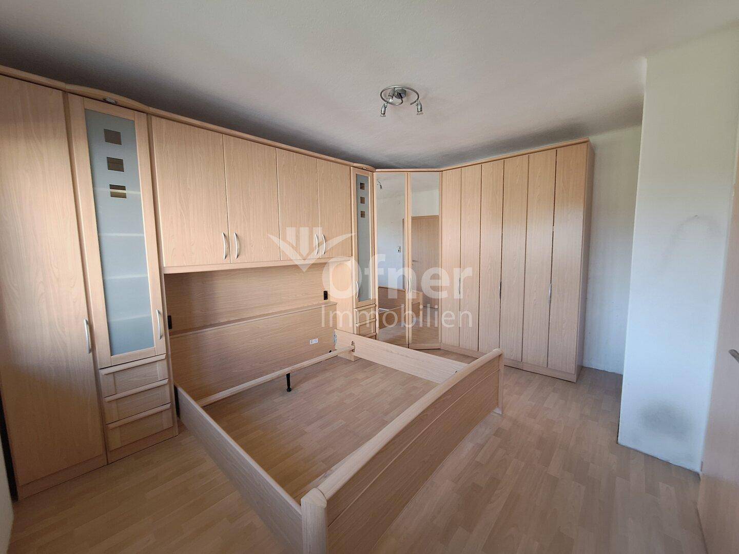 Schlafzimmer mit großem Einbauschrank und Bettrahmen aus hellem Holz.