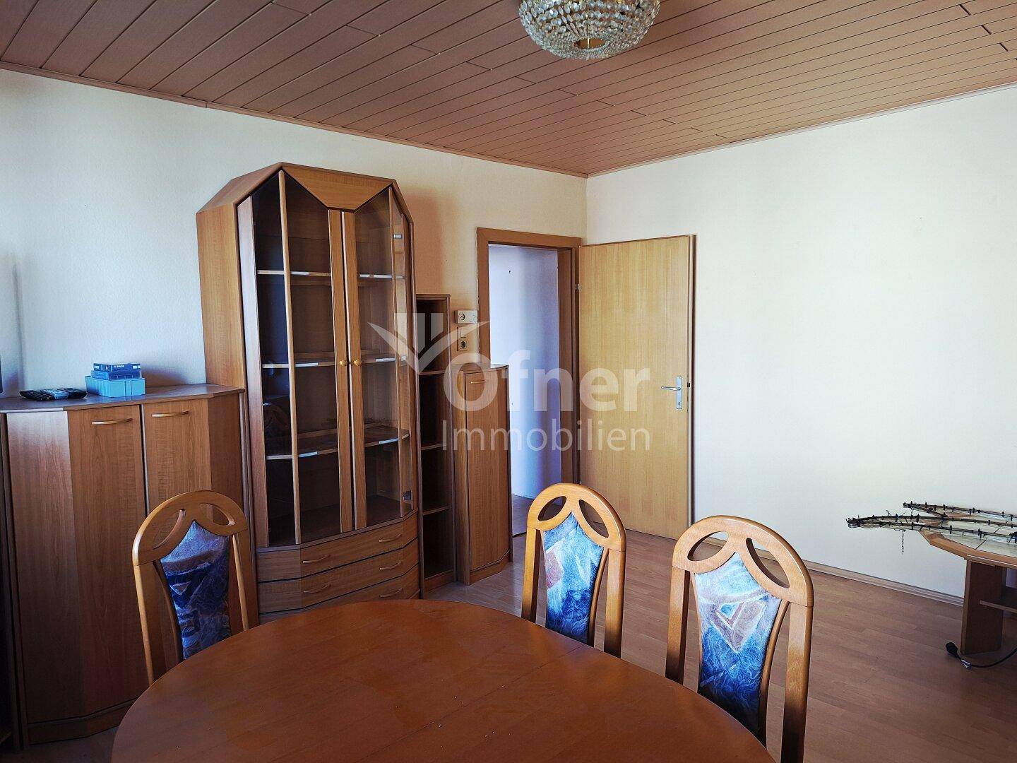 Esszimmer mit Holztisch, Stühlen und einem großen Holzschrank, unter einer Holzdecke.