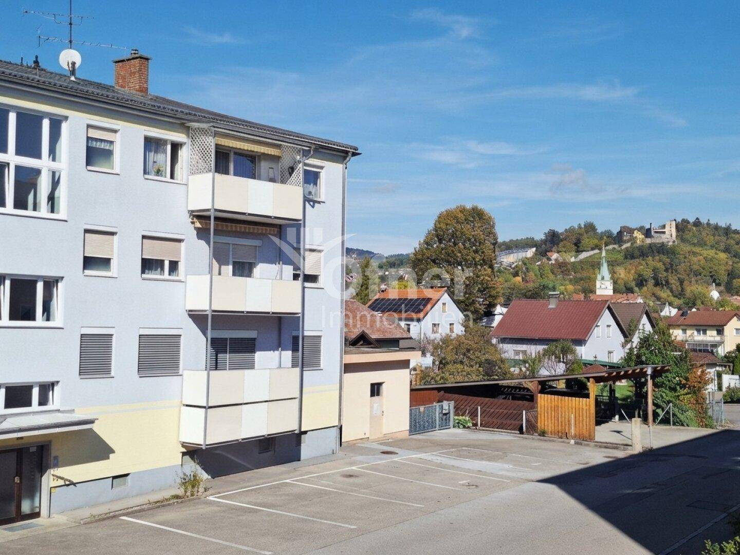 Apartmentgebäude mit Balkonen, Parkplätzen und Blick auf die umliegende Landschaft.