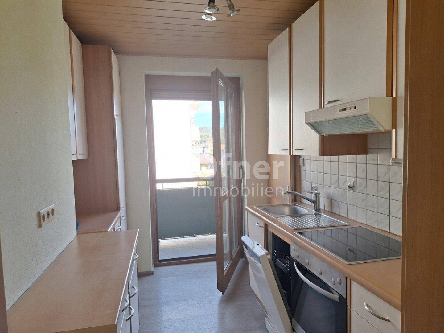 Funktionale Küche mit Einbauschränken, Spüle, Kochfeld und Zugang zum Balkon.