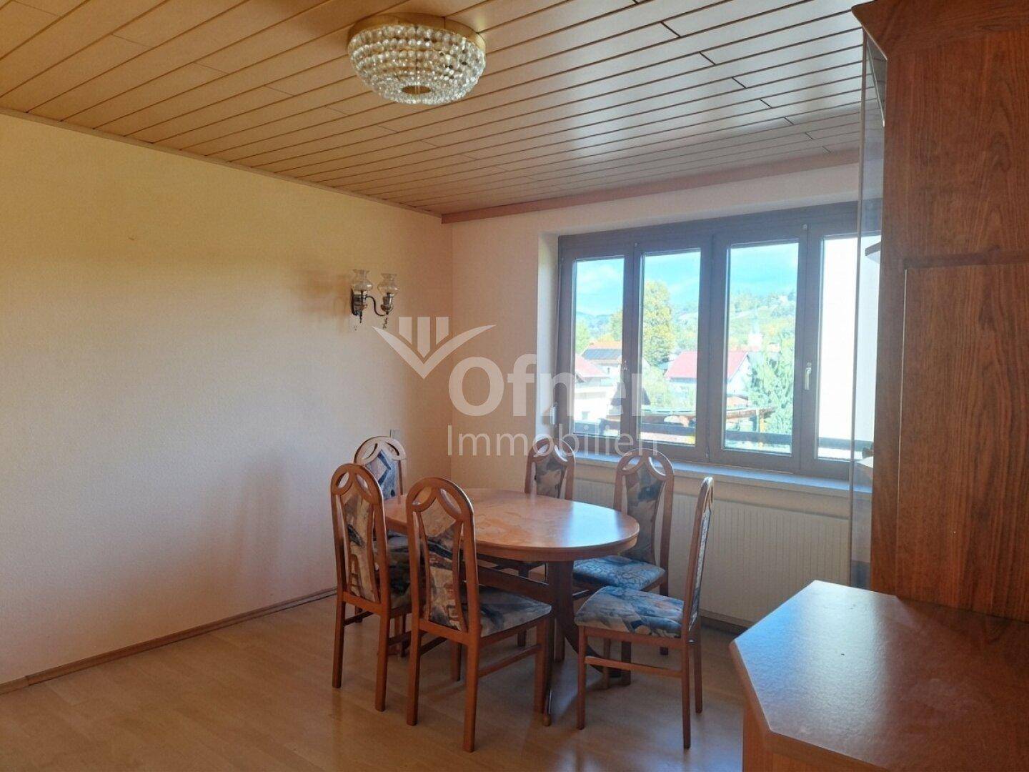 Gemütliches Esszimmer mit Holztisch, Stühlen und Blick auf die grüne Umgebung.
