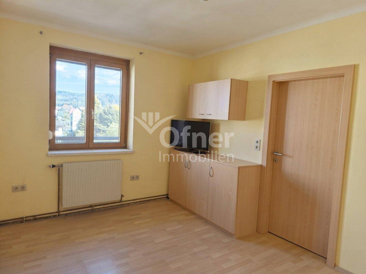 Helles Zimmer mit Holzfenster, Heizkörper und integrierten Holzschränken.