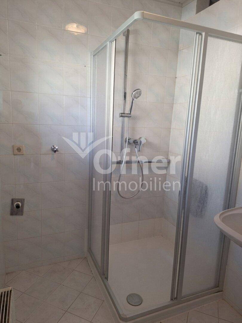 Badezimmer mit Duschkabine, weißen Fliesen und kleinem Waschbecken.