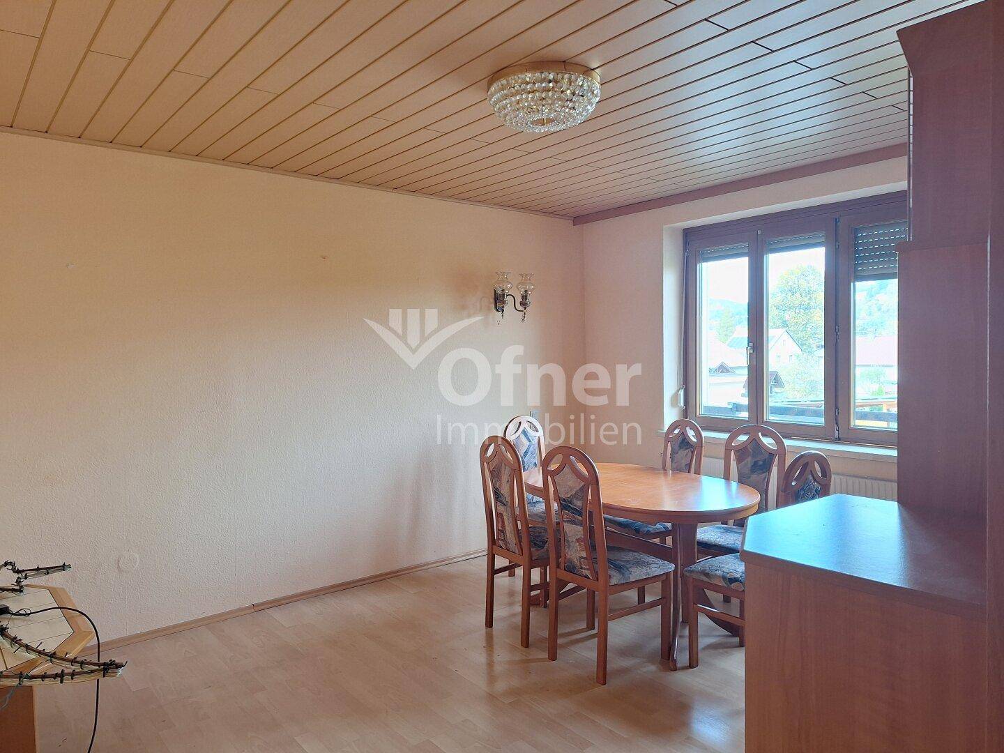 Helles Esszimmer mit Holzdecke, klassischem Esstisch und Blick ins Grüne durch große Fenster.