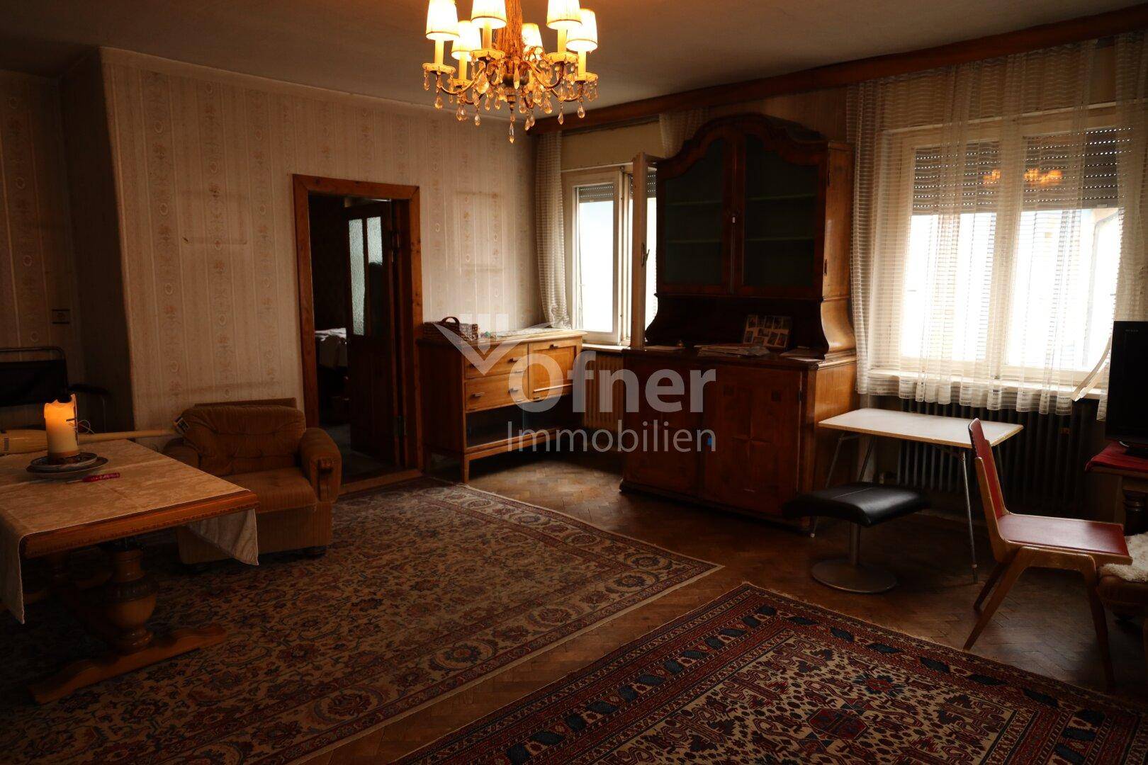 Geräumiges Wohnzimmer mit Teppichboden, Kronleuchter, vielen Pflanzen und traditionellen Möbeln.