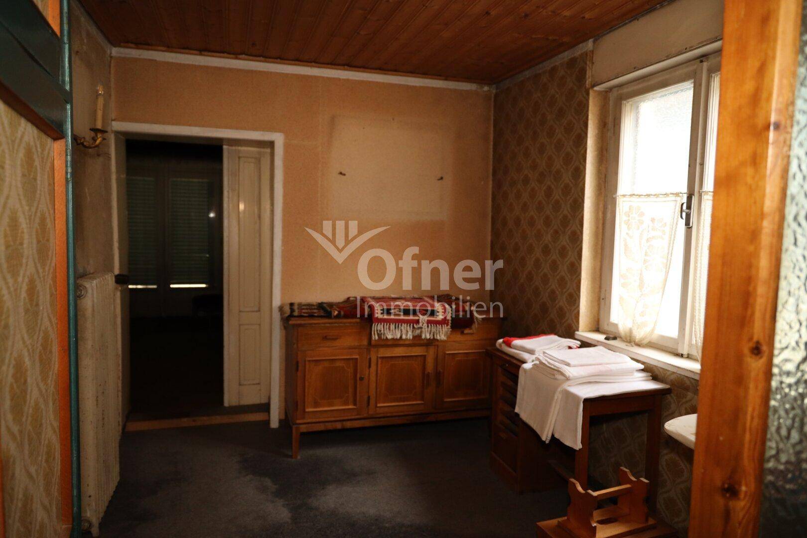Einfacher Raum mit Holzdecke, Tapeten und einem Fenster.