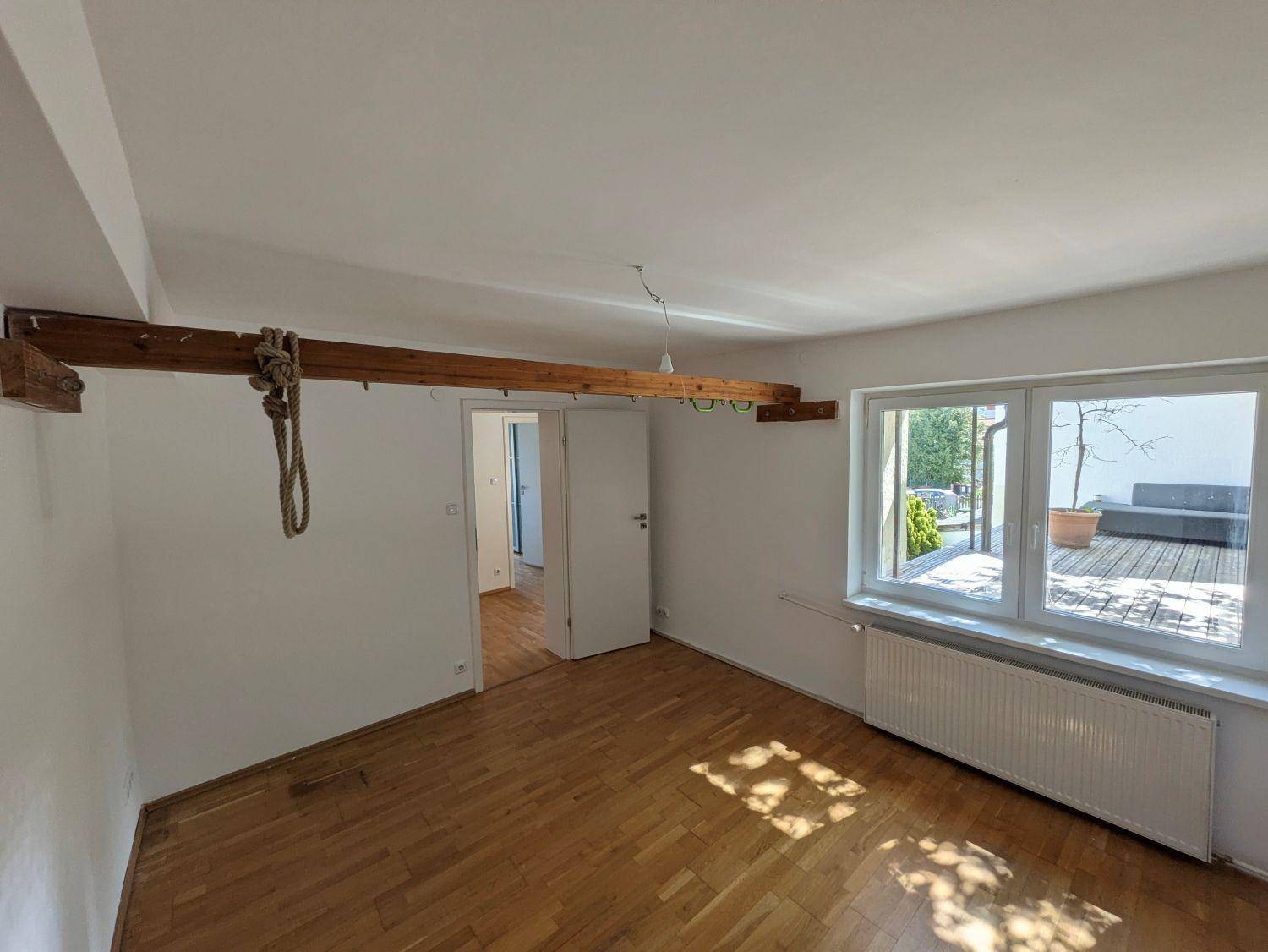 Helles Zimmer mit Parkettboden, Holzbalken und Blick auf die Holzterrasse.