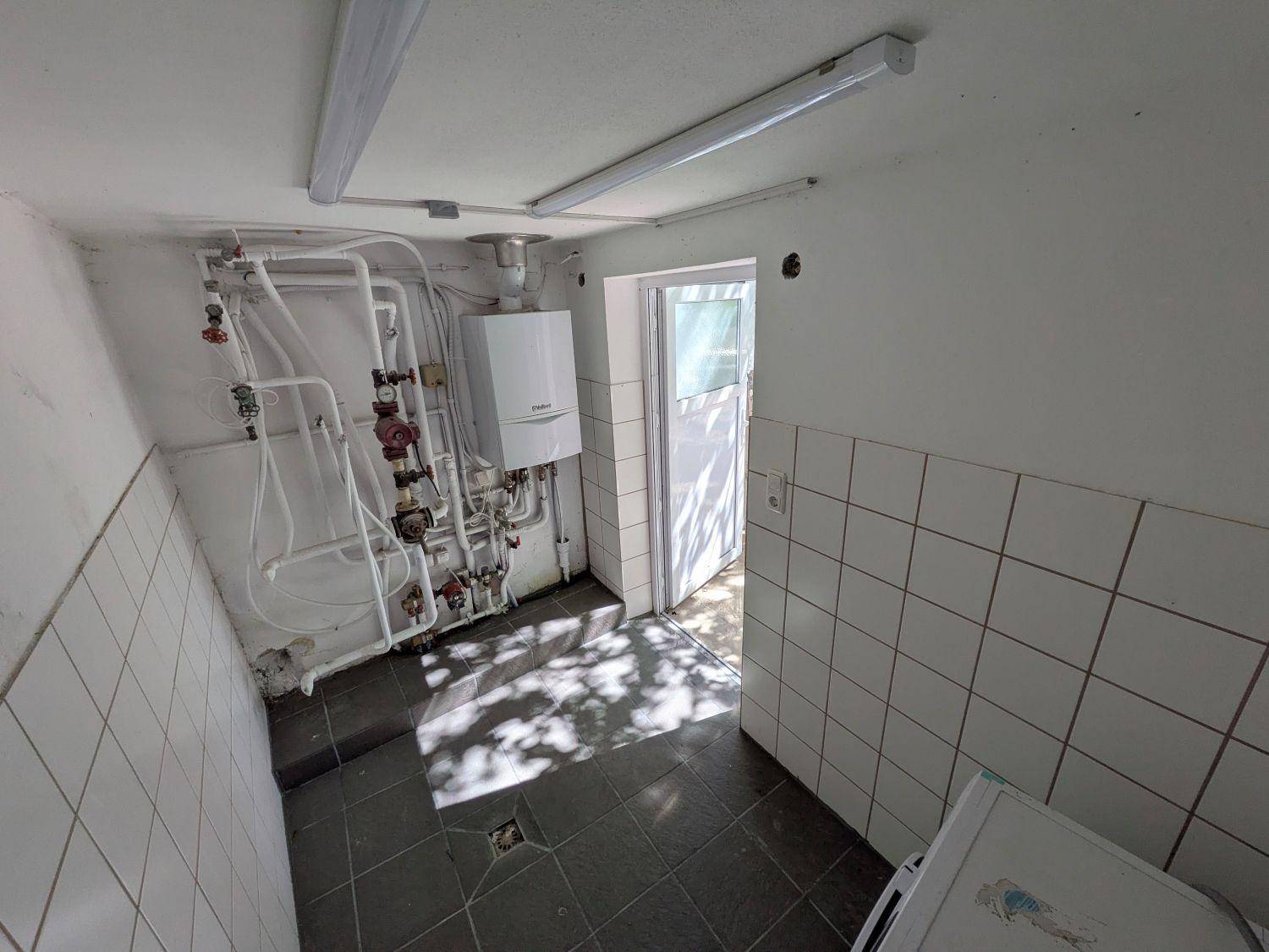 Heizungsraum im Keller mit Gastherme, Rohrleitungen und Fliesenboden.