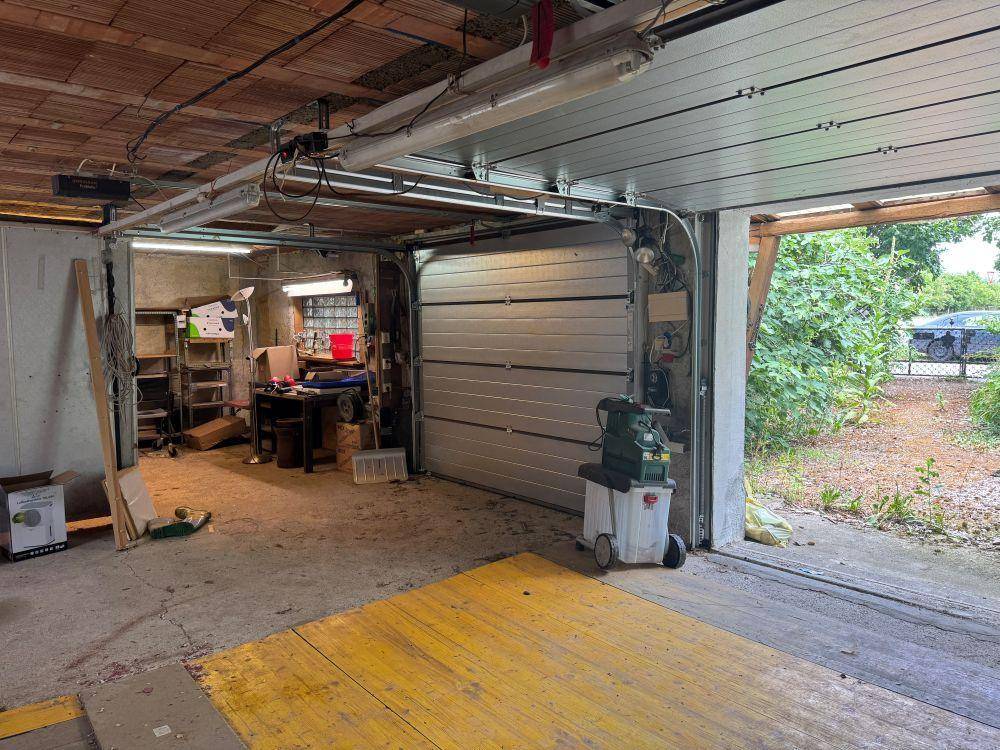 Innenansicht einer Garage mit offenem Tor, Werkzeugen und einem Arbeitsbereich, der zum Garten führt.