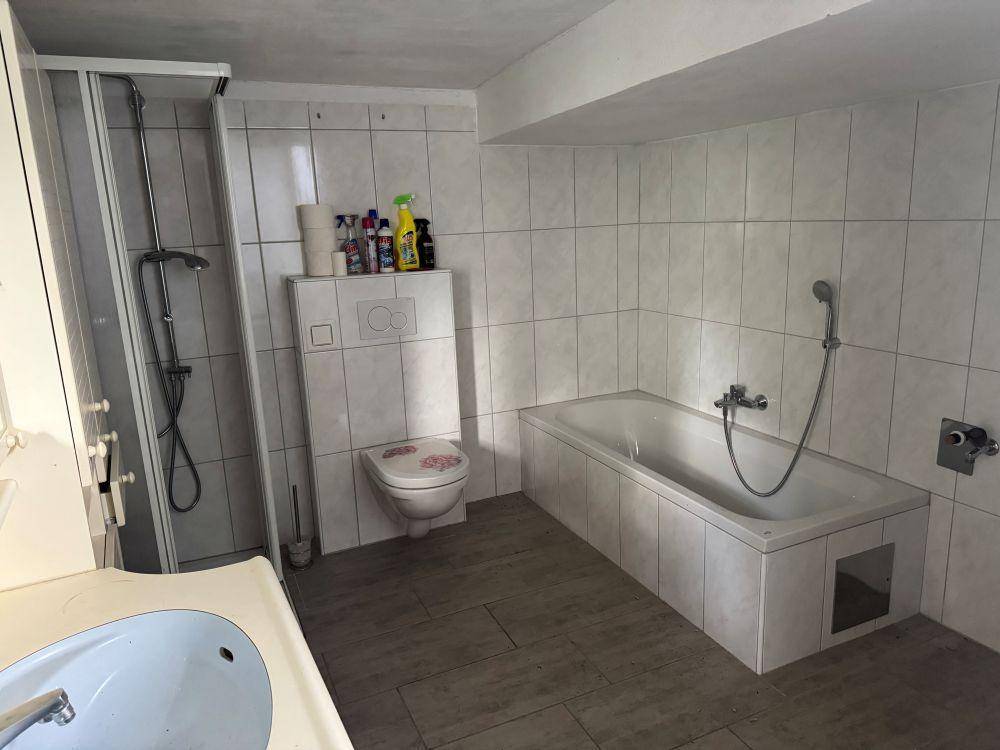 Badezimmer mit Badewanne, Duschkabine und weißen Fliesen an den Wänden, sowie einem Waschbecken.
