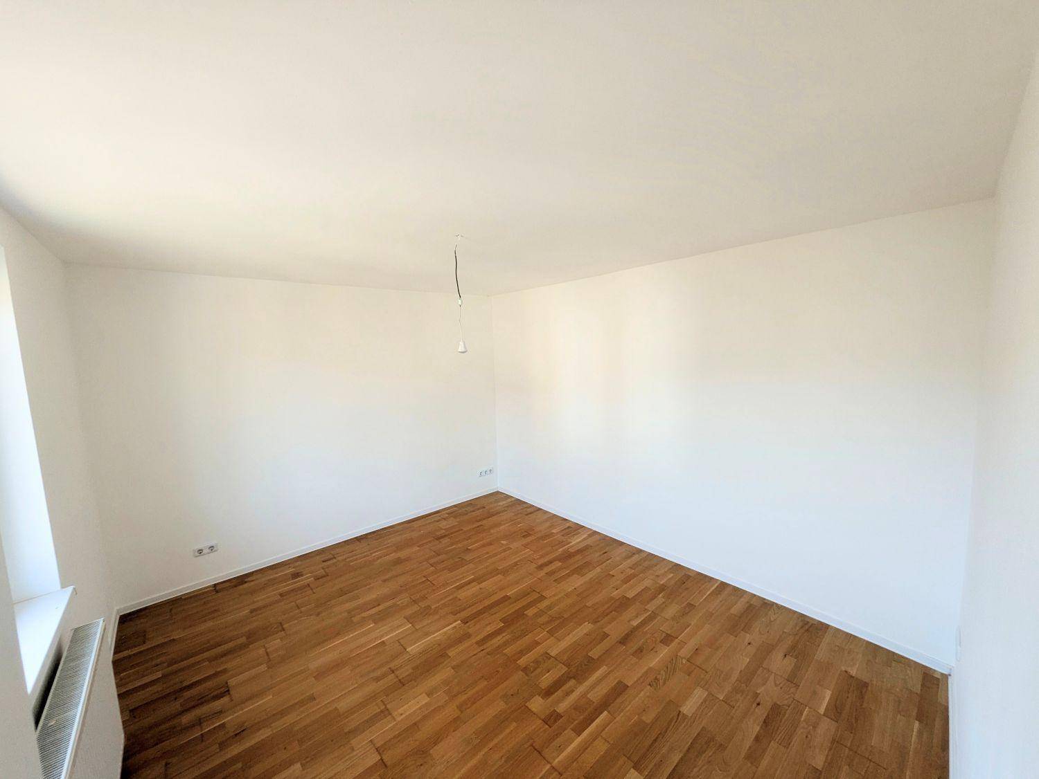 Helles Zimmer mit Parkettboden und weißen Wänden, ideal als Schlaf- oder Arbeitszimmer.