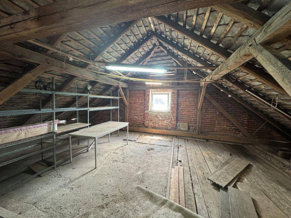 Unausgebauter Dachboden mit sichtbaren Holzbalken, einem kleinen Fenster und Lagerregalen.