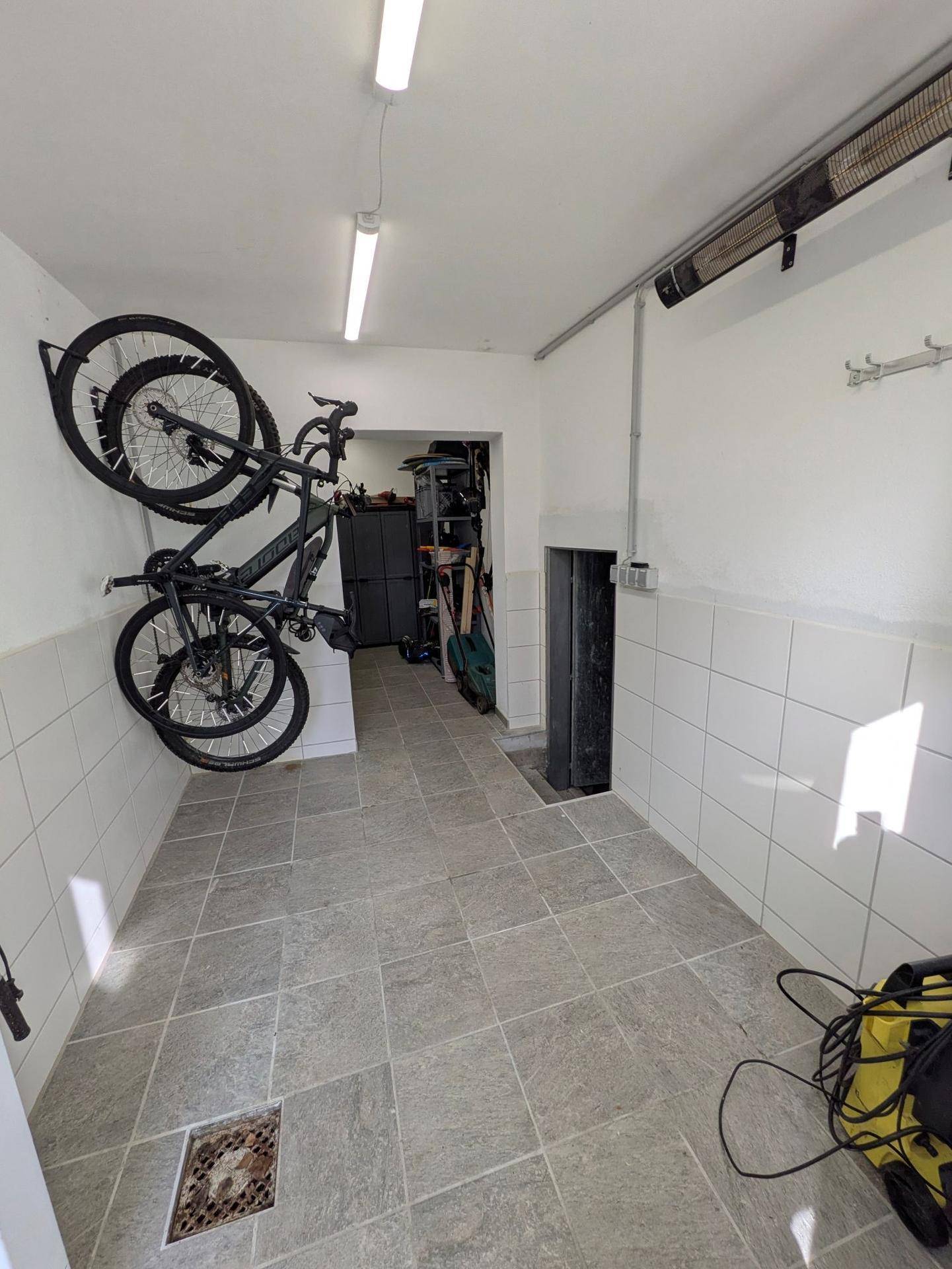 Geräumiger Abstellraum mit Fliesenboden und praktischer Fahrradaufhängung an der Wand.