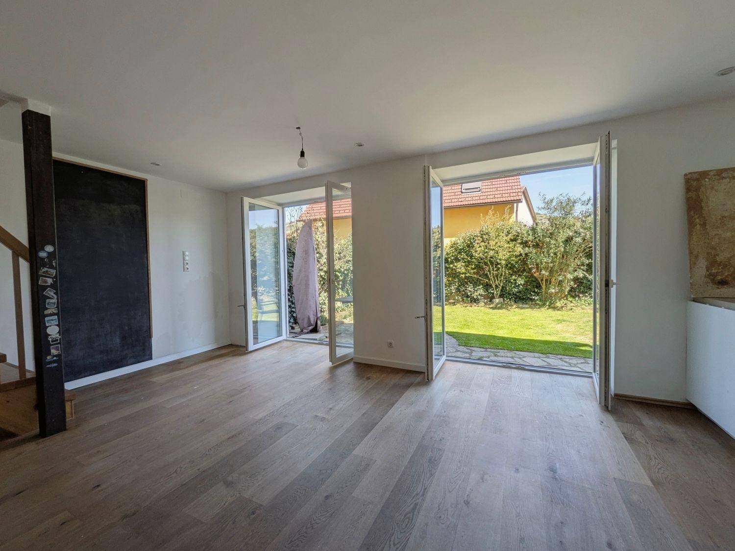 Geräumiger Wohnbereich mit Holzboden und großen Fenstertüren zum Garten.
