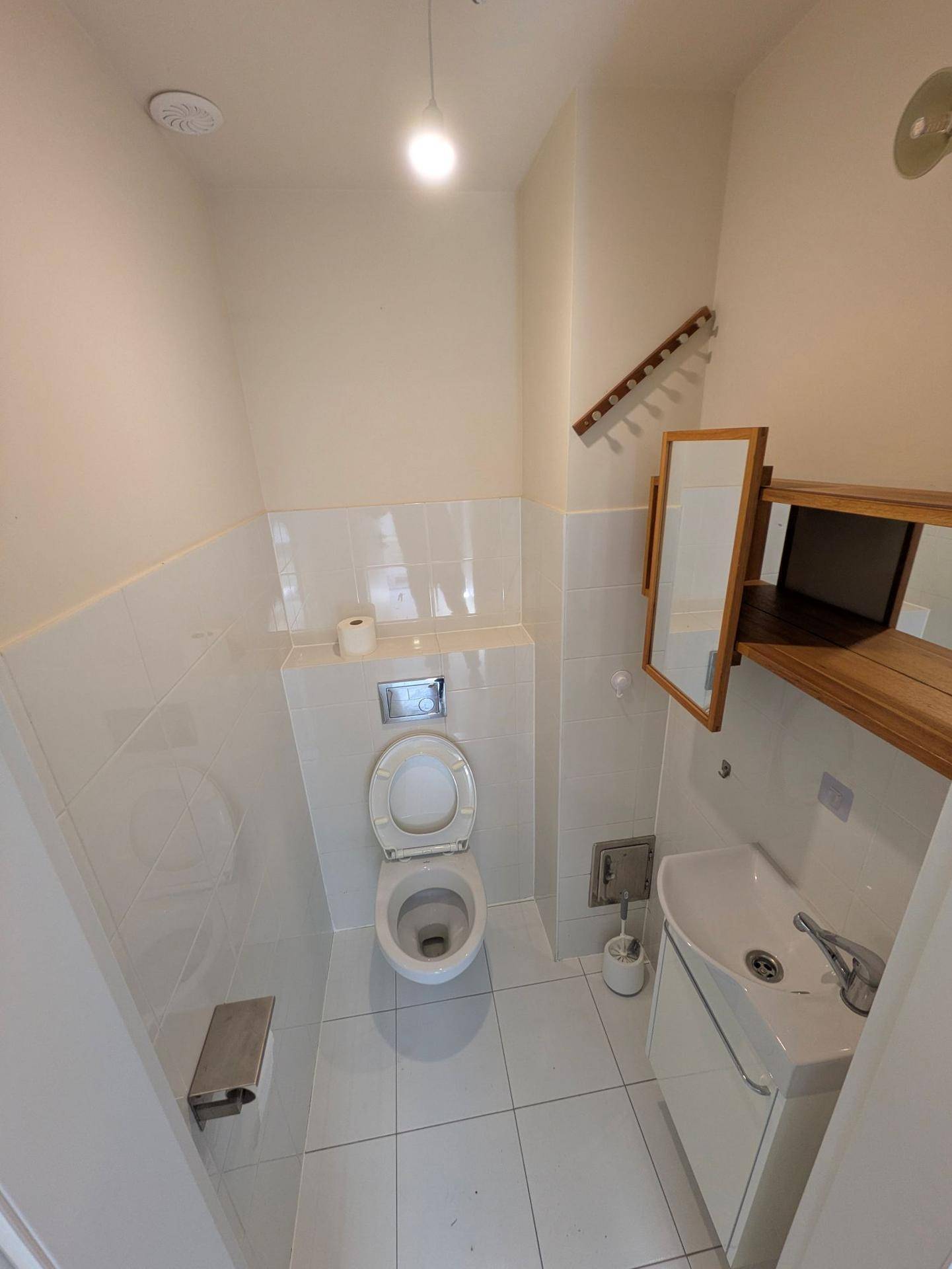 Kleines Gäste-WC mit weißen Fliesen, wandhängendem WC und modernem Waschtisch.