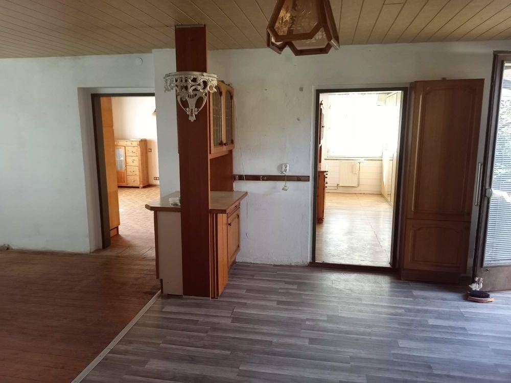 Innenraum mit Holzbalkendecke, Laminatboden und einem hölzernen Einbauschrank, der zu weiteren Räumen führt.