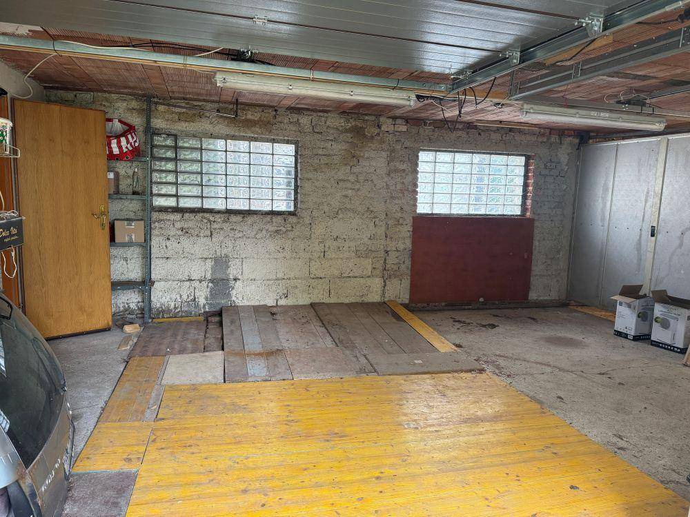 Innenansicht einer Garage mit Betonwänden, Glasbausteinfenstern und Holzbrettern auf dem Boden.