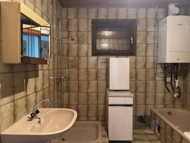 Badezimmer mit braunen Fliesen, Badewanne, Dusche und einem Warmwasserbereiter an der Wand.
