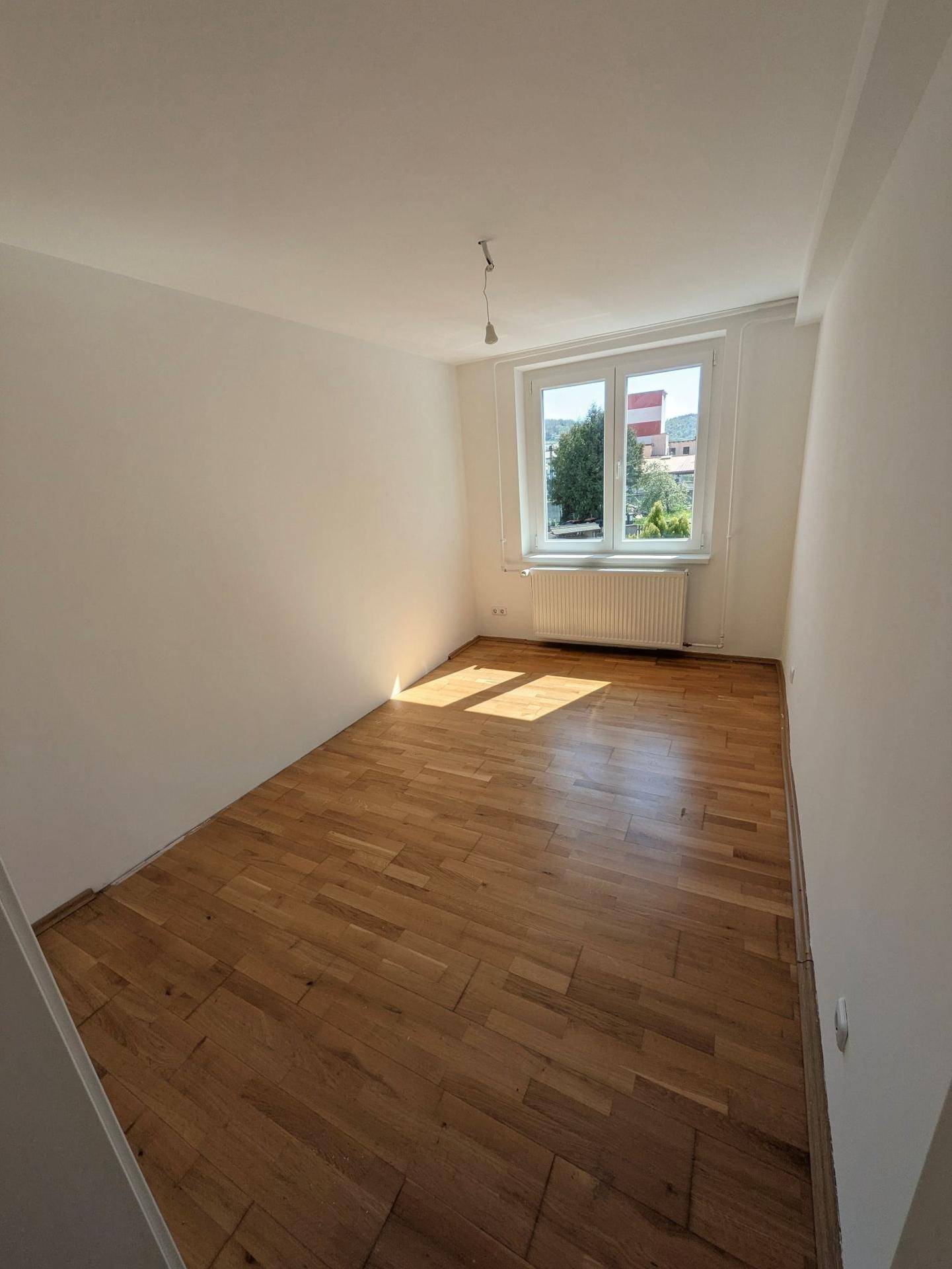 Helles Zimmer mit Parkettboden und Fenster, bereit zur individuellen Gestaltung.