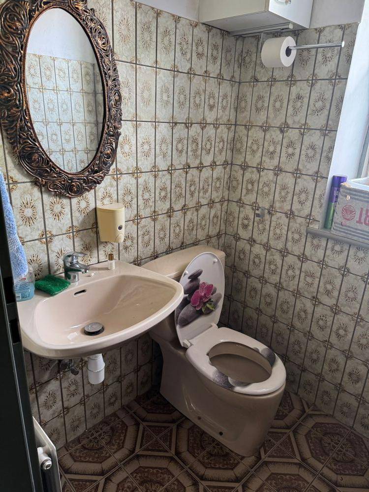 Kleines WC mit gemusterten Fliesen an Wänden und Boden, ausgestattet mit Waschbecken und Toilette.