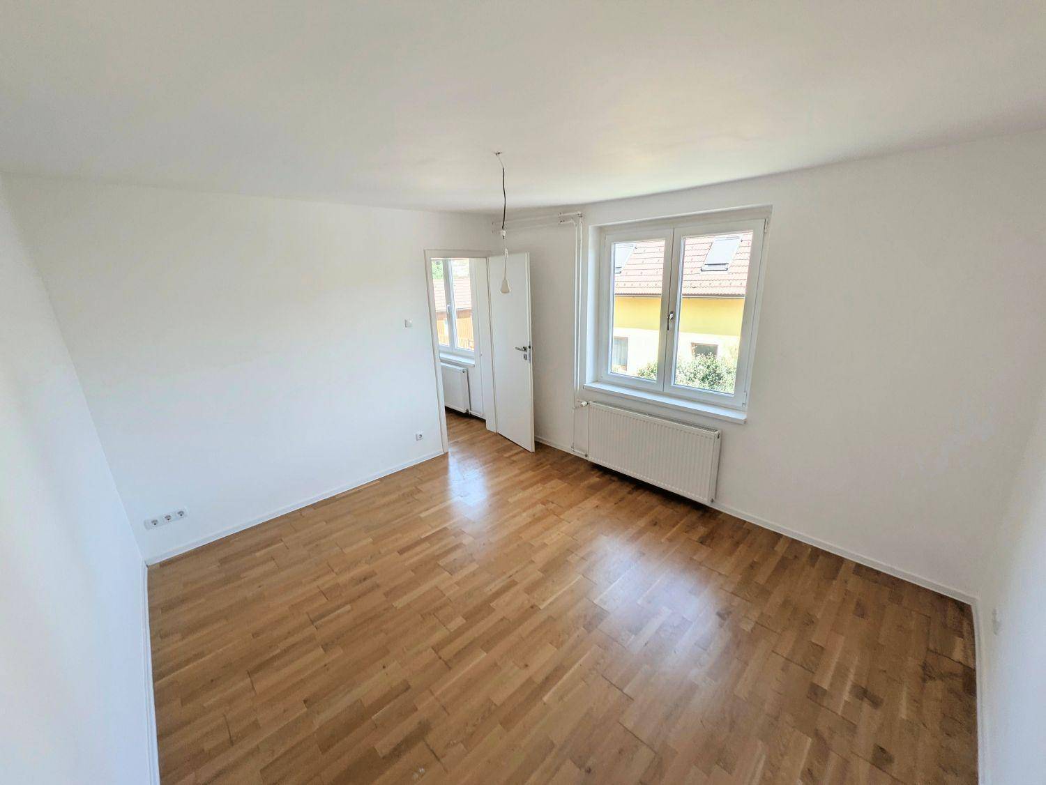 Lichtdurchflutetes Zimmer mit Parkettboden, Fenster und Heizkörper.