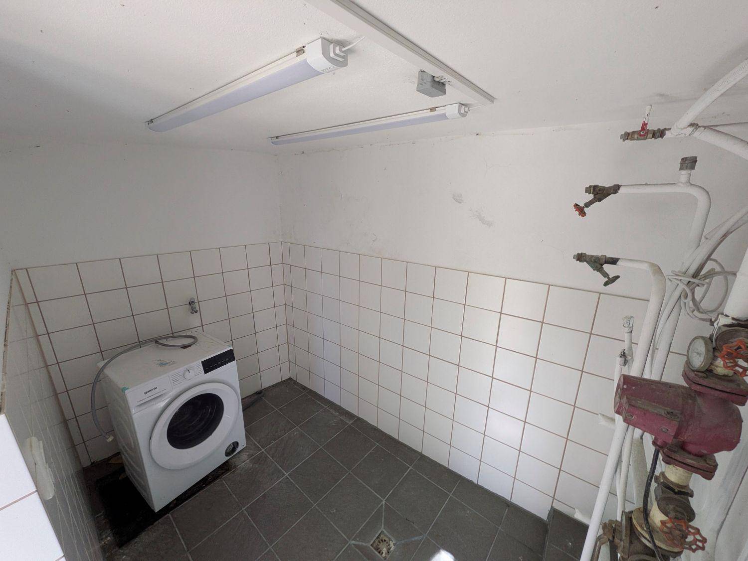 Waschküche im Keller mit Waschmaschine und gefliesten Wänden und Böden.