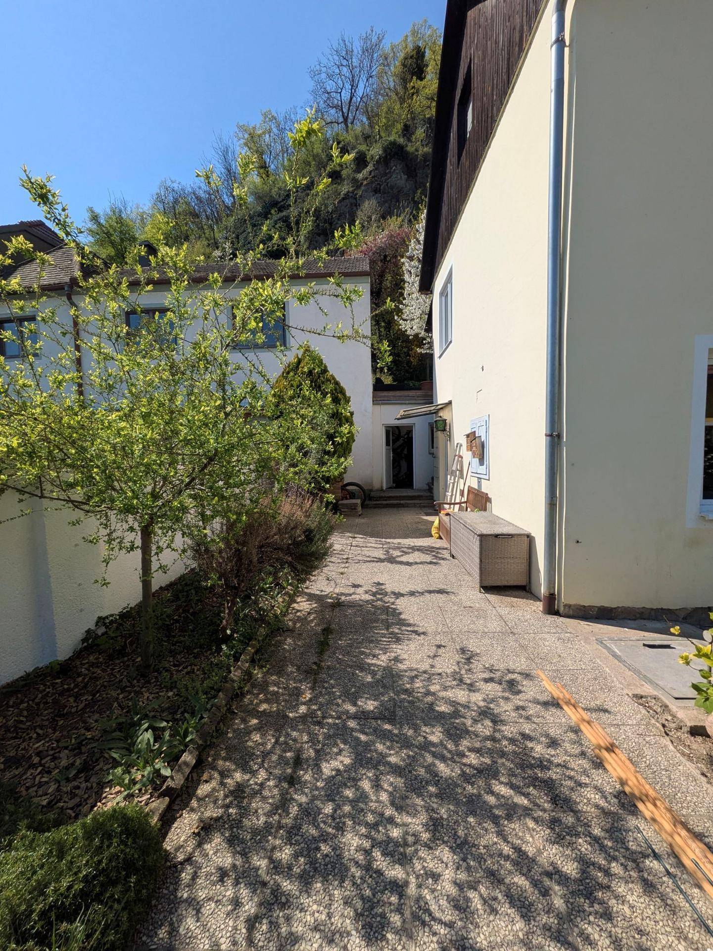 Gepflasterter Weg zwischen zwei Gebäuden mit leichter Hanglage und Bäumen.