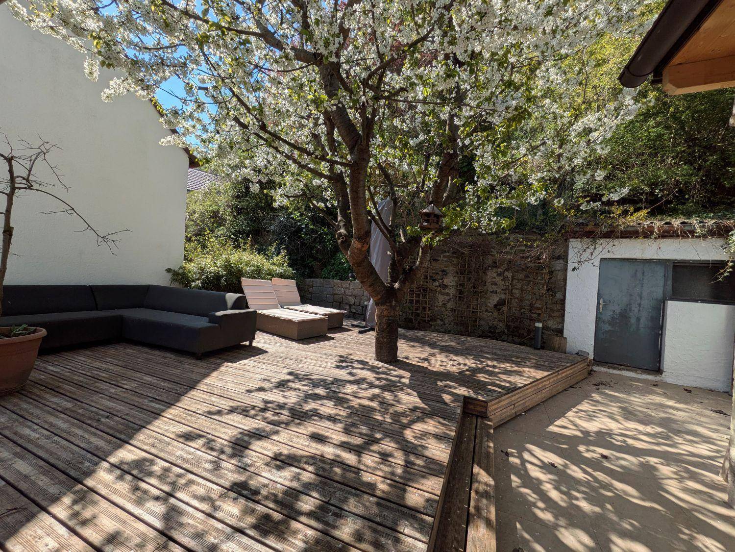 Holzterrasse mit blühendem Baum und bequemen Lounge-Möbeln für entspannte Stunden im Freien.
