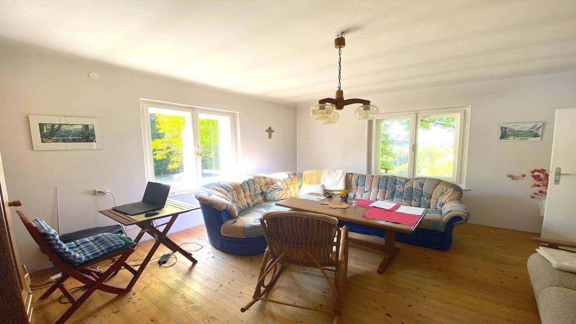Helles Wohnzimmer mit Holzboden, bequemen Sofas und großen Fenstern mit Blick ins Grüne.