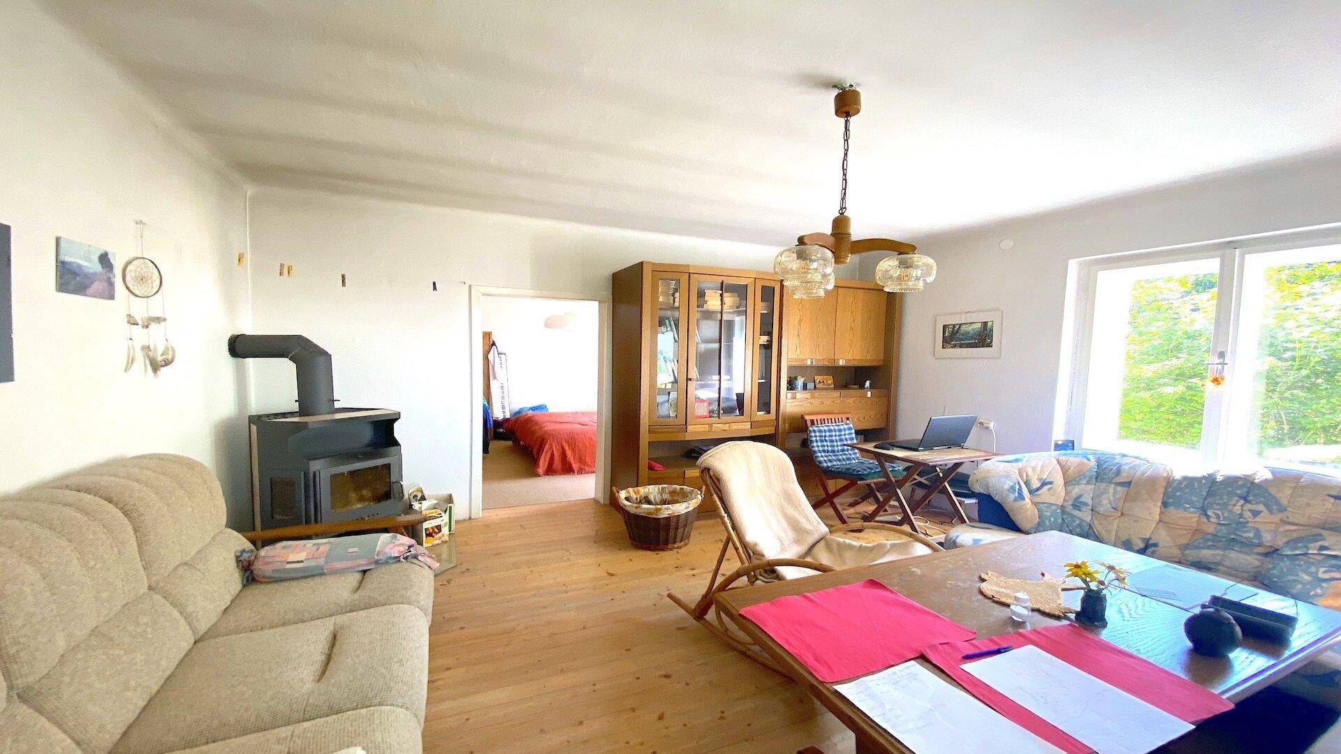 Gemütliches Wohnzimmer mit Holzboden, Kaminofen und Zugang zu einem weiteren Raum.