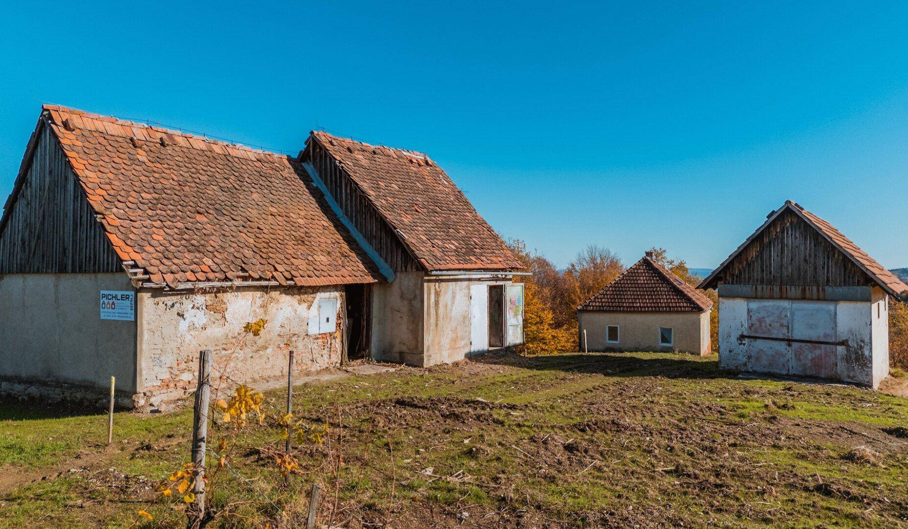 Rustikale ländliche Gebäude mit alten Ziegeldächern und verputzten Wänden unter strahlend blauem Himmel.