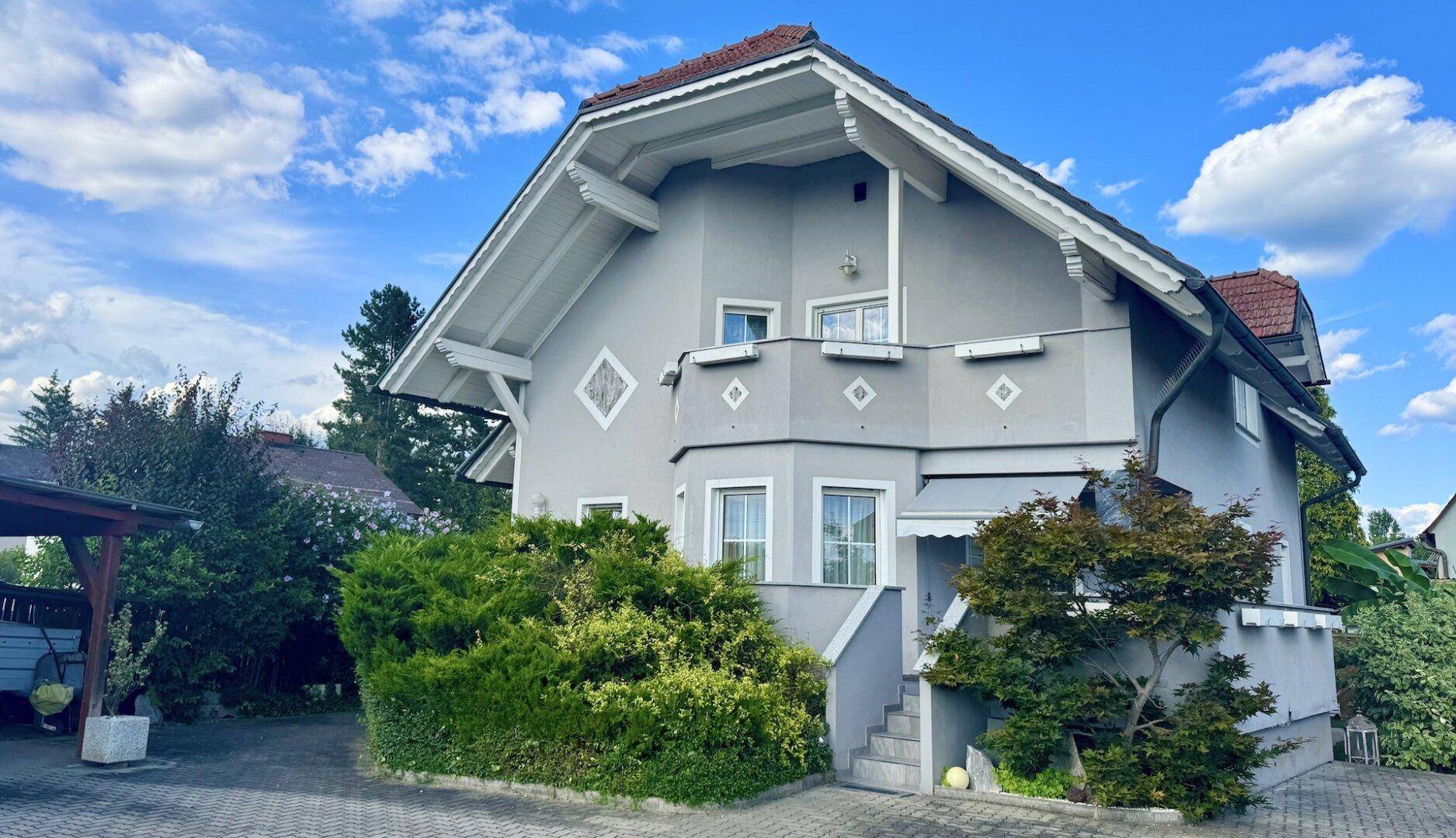 Ansicht des Einfamilienhauses mit gepflegter Fassade, Carport und üppiger Bepflanzung.