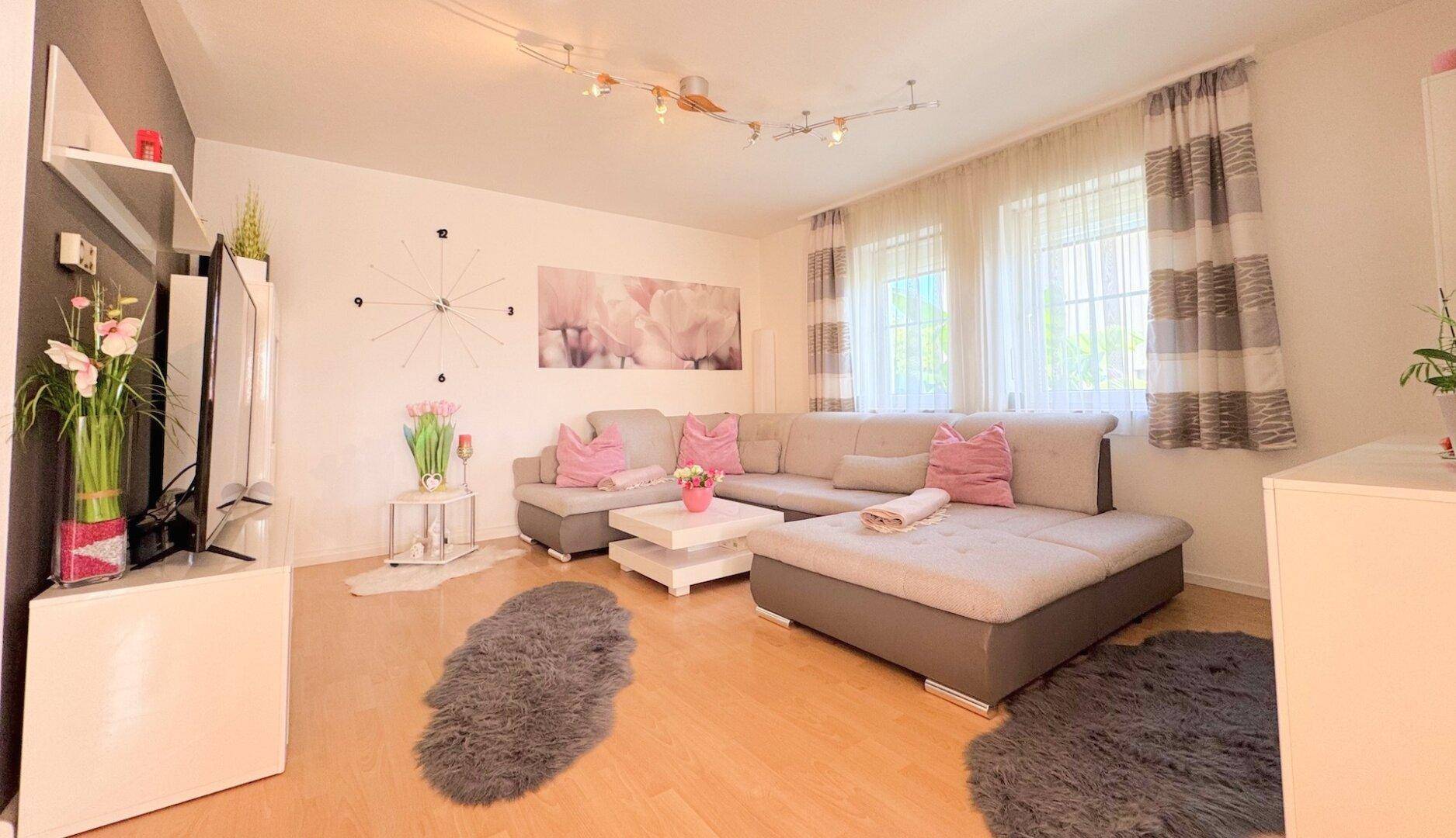 Helles Wohnzimmer mit großem Ecksofa, Holzboden und moderner Dekoration in Rosatönen.