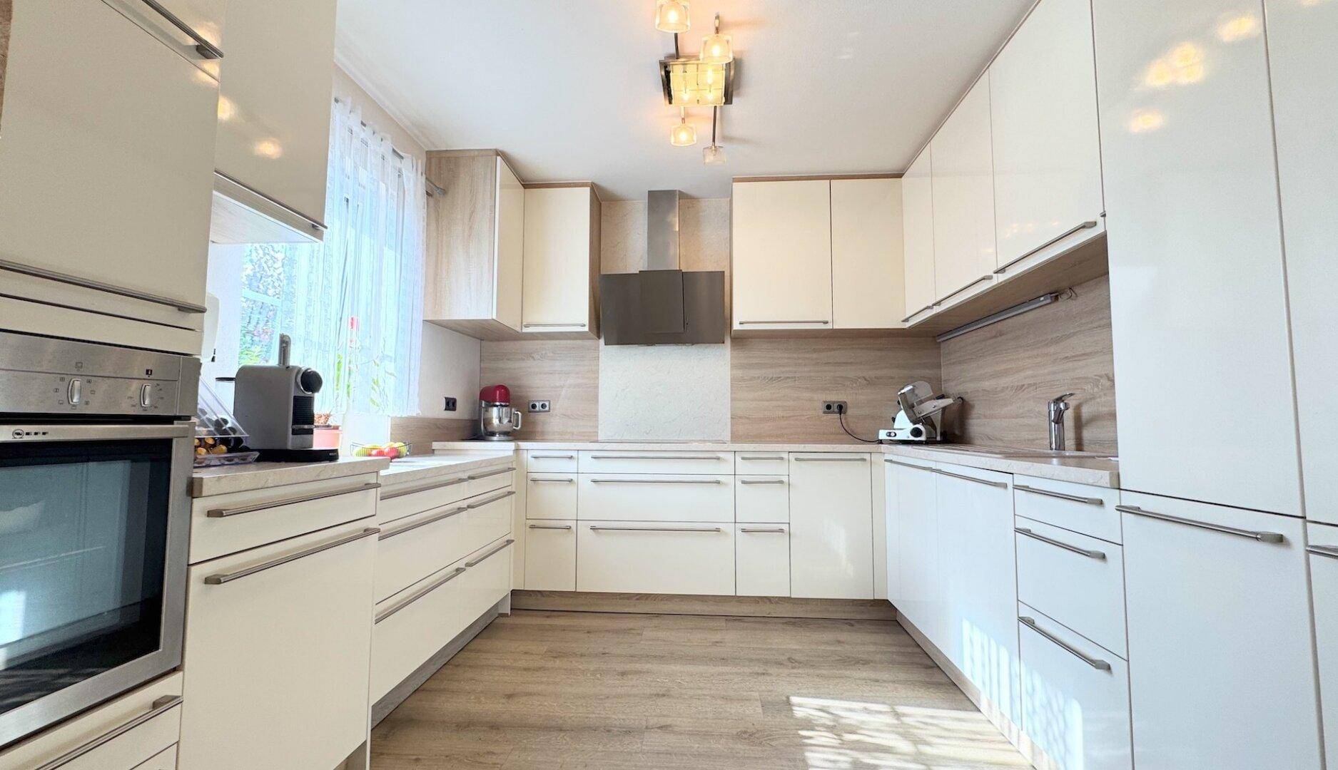 Moderne Einbauküche mit hellen Hochglanzfronten, integrierten Geräten und Holzboden.