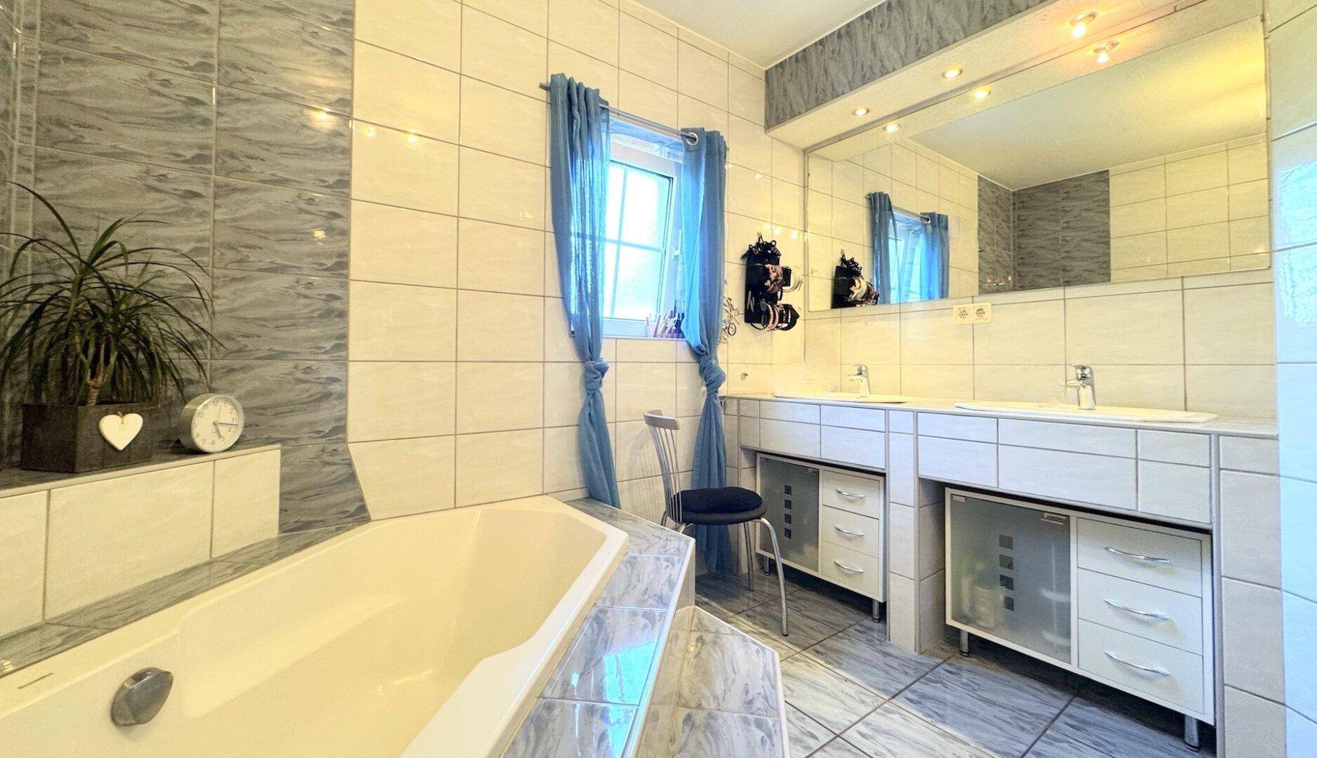 Geräumiges Badezimmer mit Badewanne, Doppelwaschbecken und hellgrauen Fliesen.