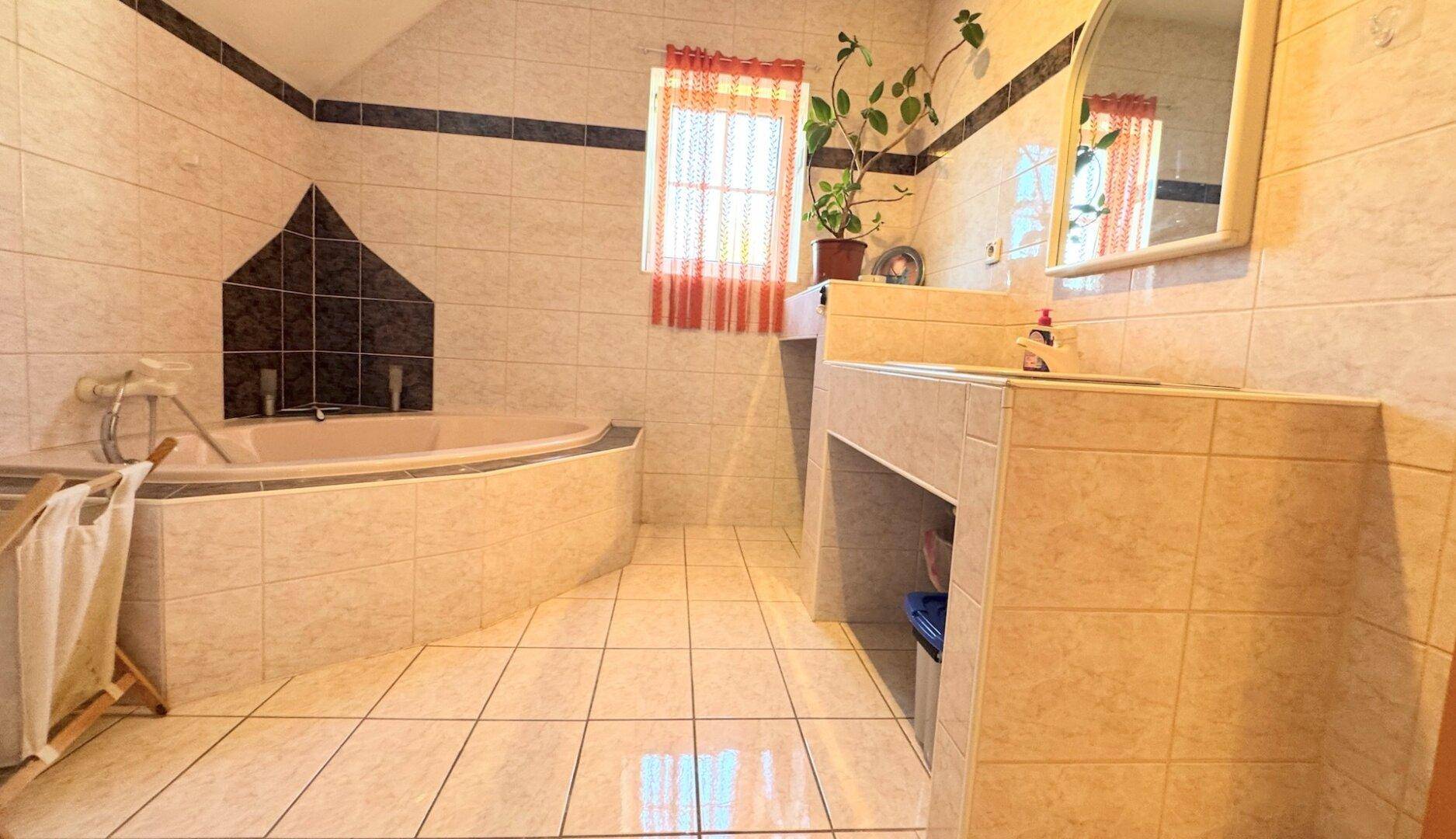 Helles Badezimmer mit Eckbadewanne, Einzelwaschbecken und Fenster.