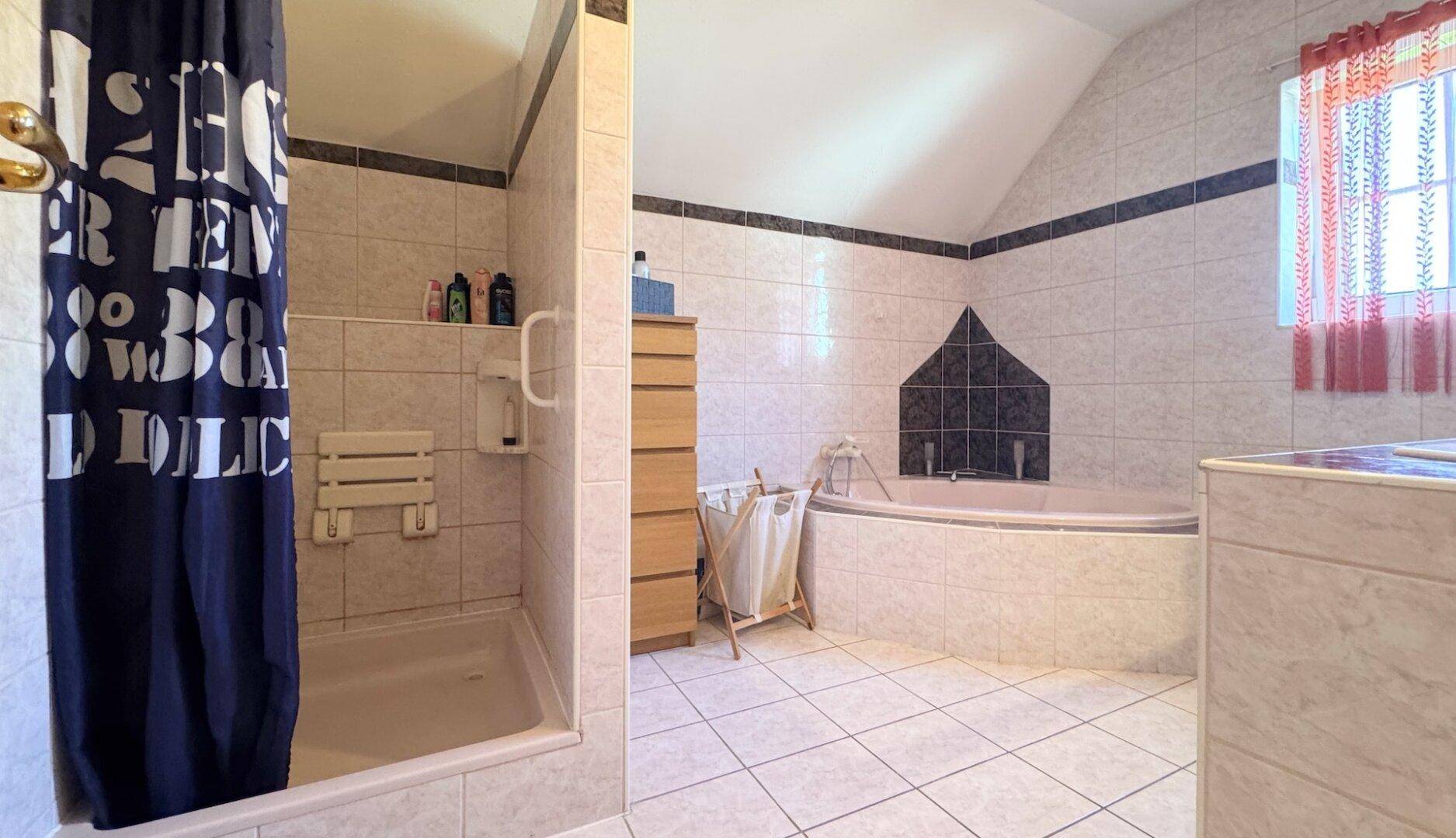 Badezimmer mit Dusche, Eckbadewanne und hellen Fliesen unter Dachschrägen.