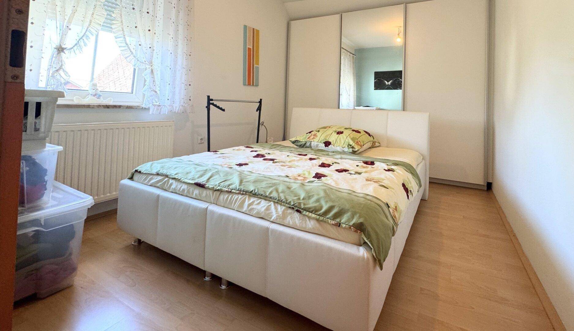Schlafzimmer mit Doppelbett, Spiegelschrank und Laminatboden.
