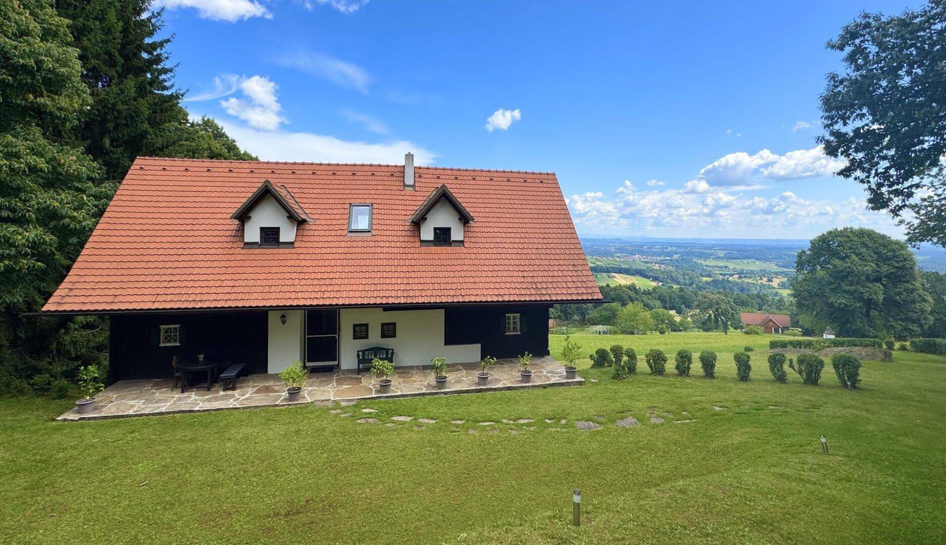 Charmantes Landhaus mit rotem Ziegeldach und einer gepflasterten Terrasse mit weitem Ausblick.