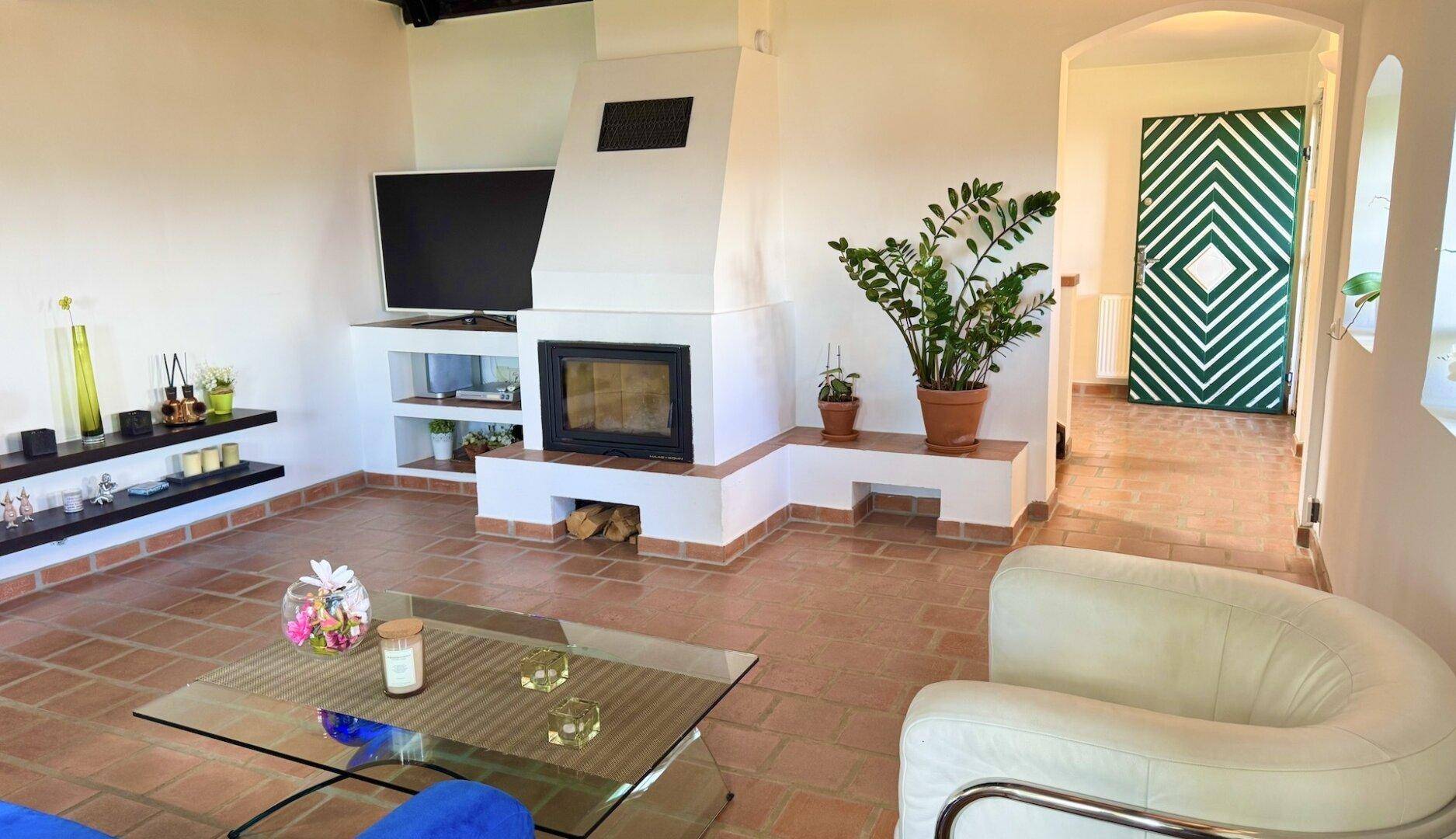 Gemütliches Wohnzimmer mit Kamin, Terrakottaboden und einem Fernseher über dem Kaminsims.