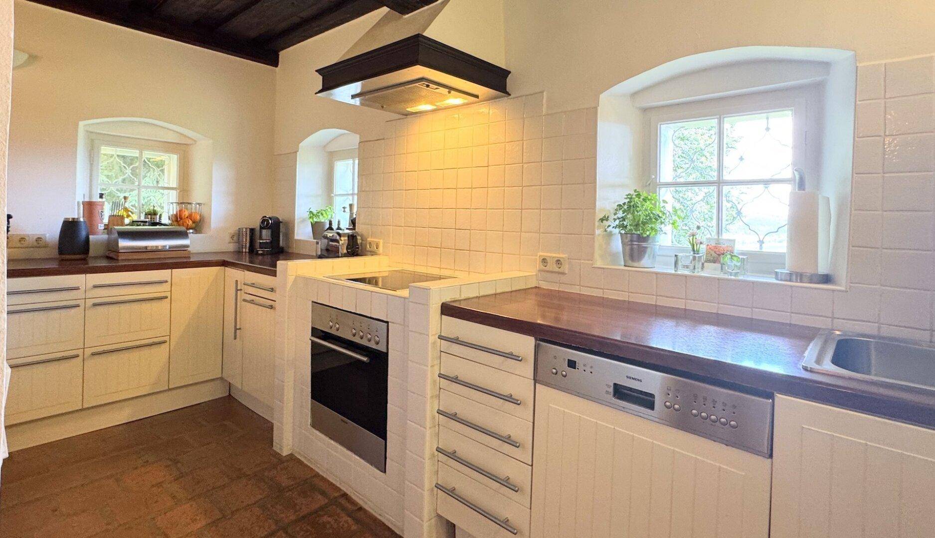 Traditionelle Küche mit weißen Fliesen, Holzarbeitsplatten und integrierten Geräten unter einem Fenster.