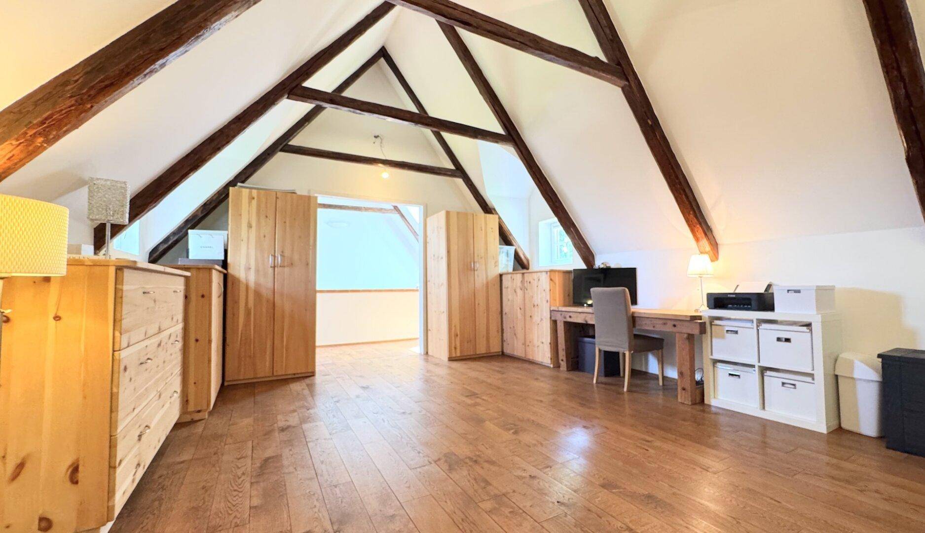 Geräumiges Dachgeschosszimmer mit Holzboden, freiliegenden Balken und viel Platz für Büro oder Hobby.