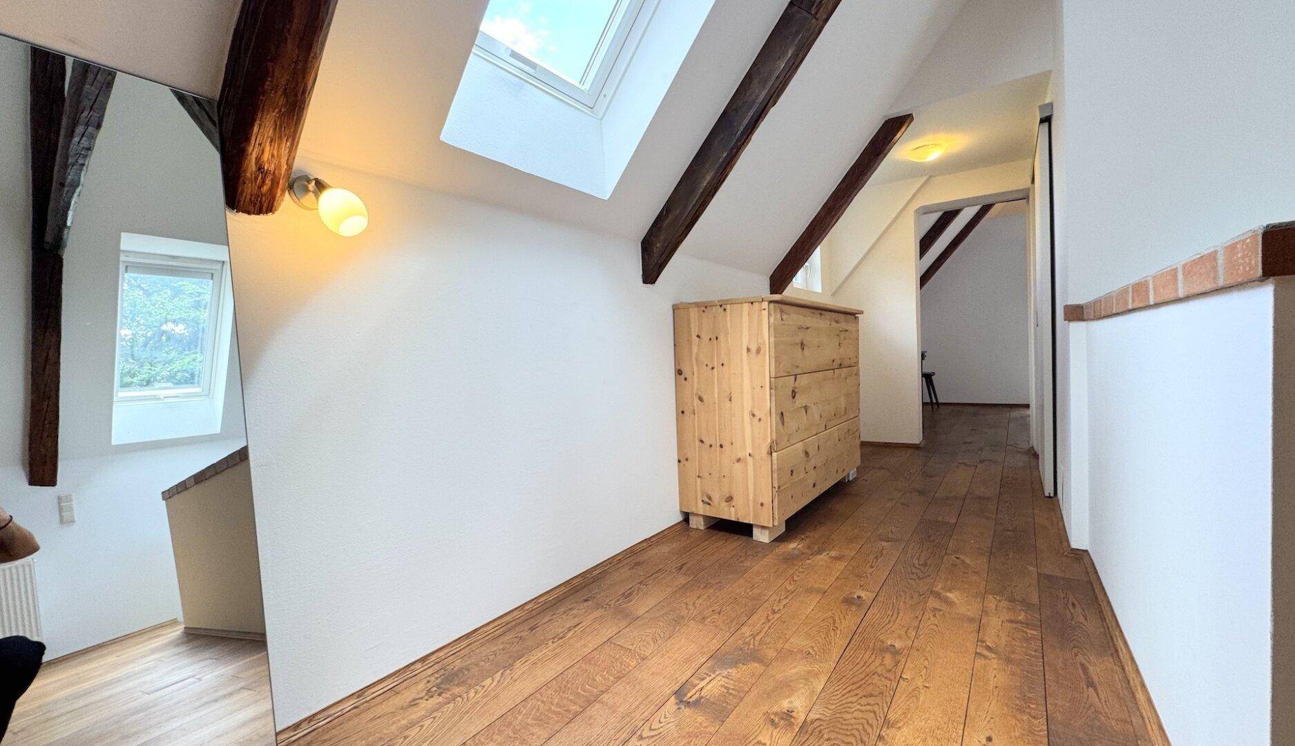 Heller Flur im Dachgeschoss mit Holzboden, sichtbaren Balken und einem Dachfenster für natürliches Licht.